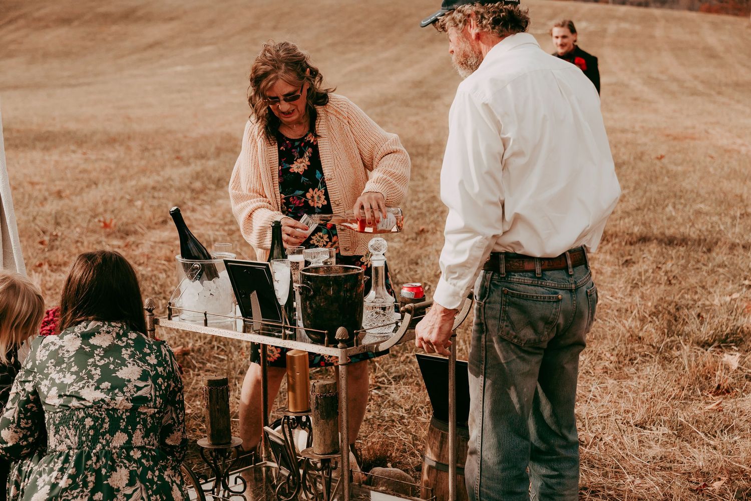 Guests enjoying champagne service at an outdoor rustic wedding bar cart in an autumn countryside setting.