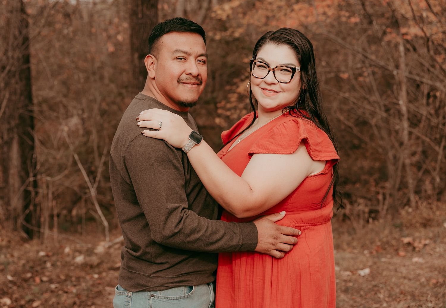 Couple embracing warmly in front of colorful autumn forest backdrop.