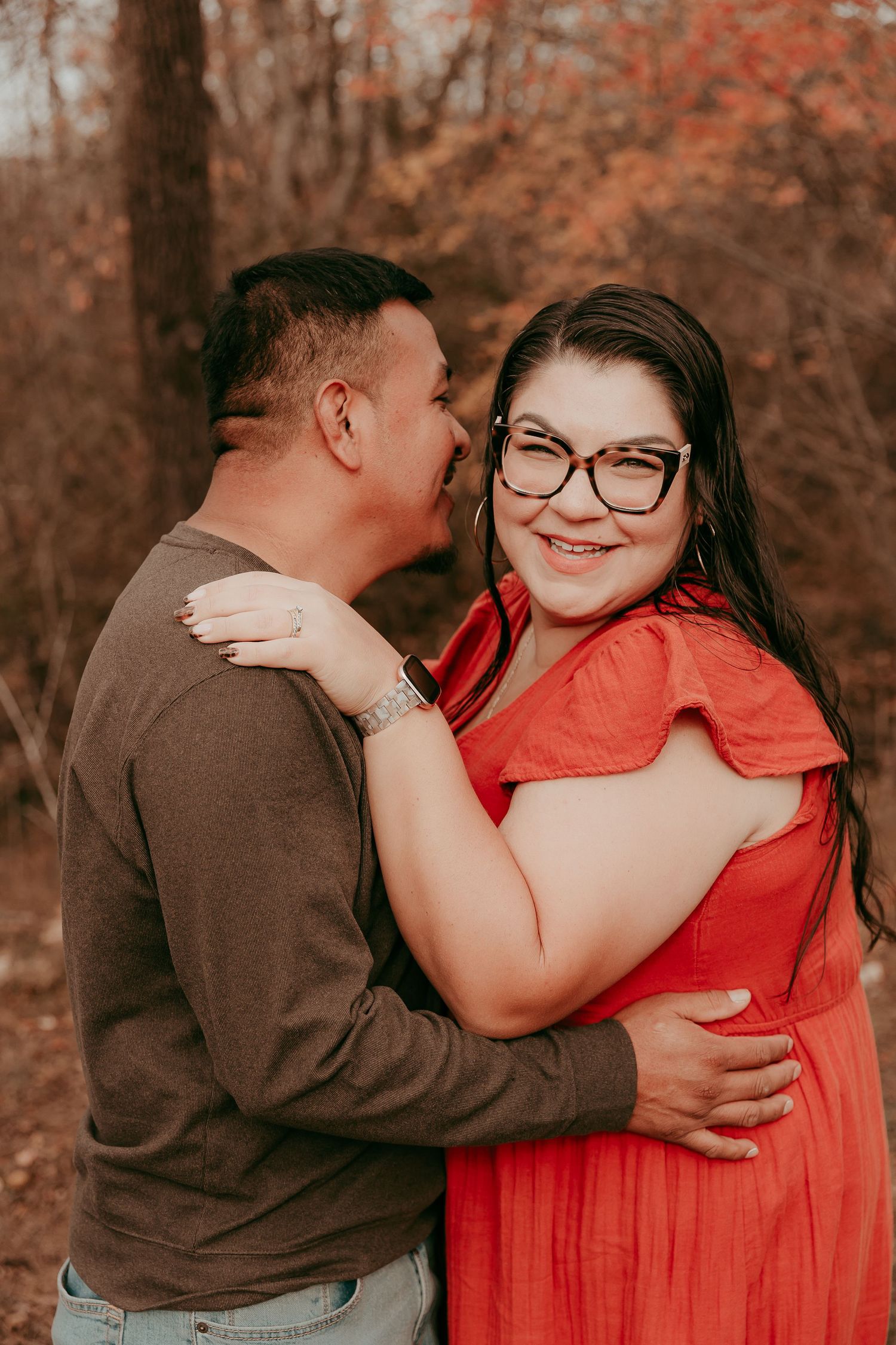 Man whispering to smiling woman in red dress during fall couples photo session.