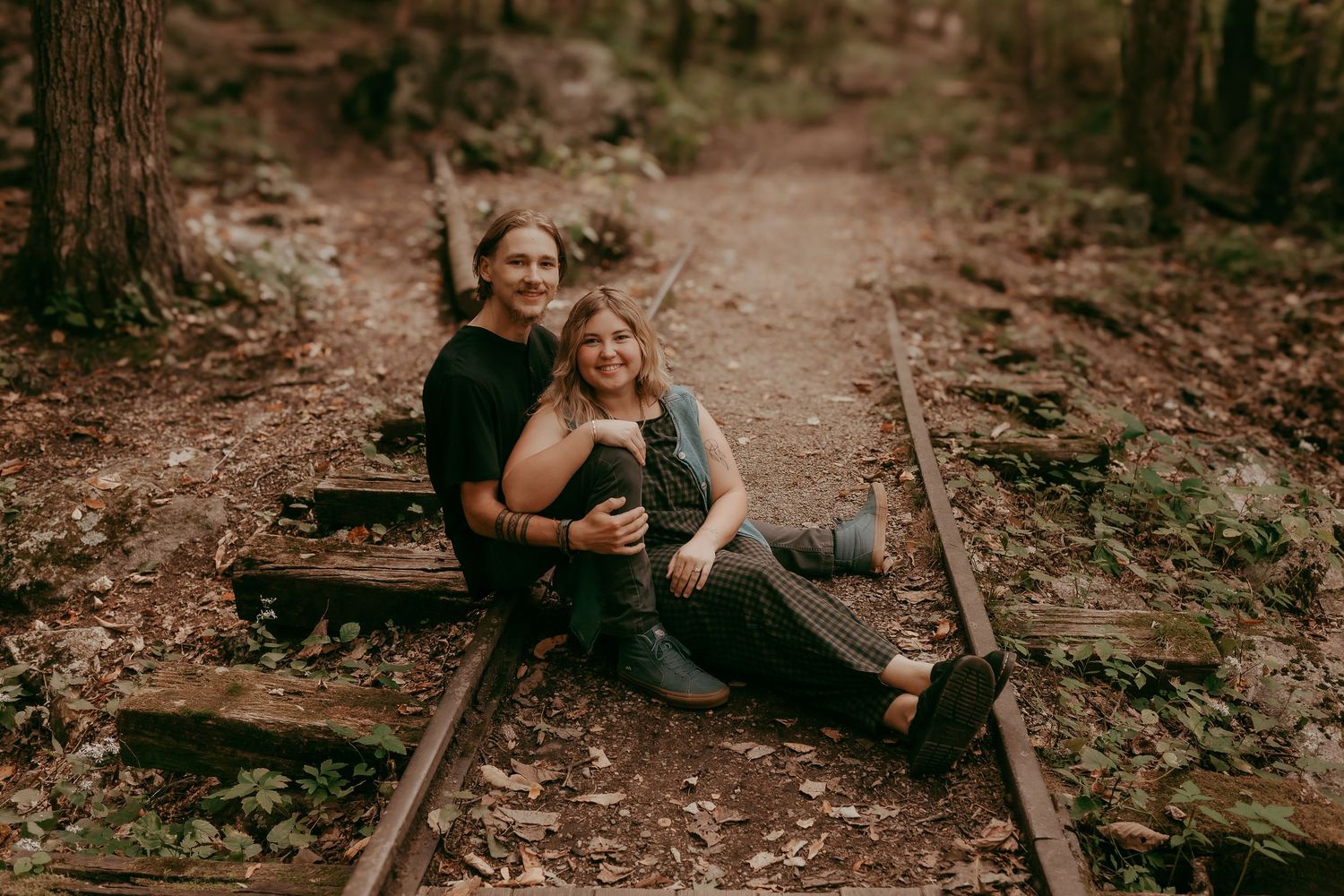 Couple sitting together on old forest railway tracks smiling and laughing outdoors.