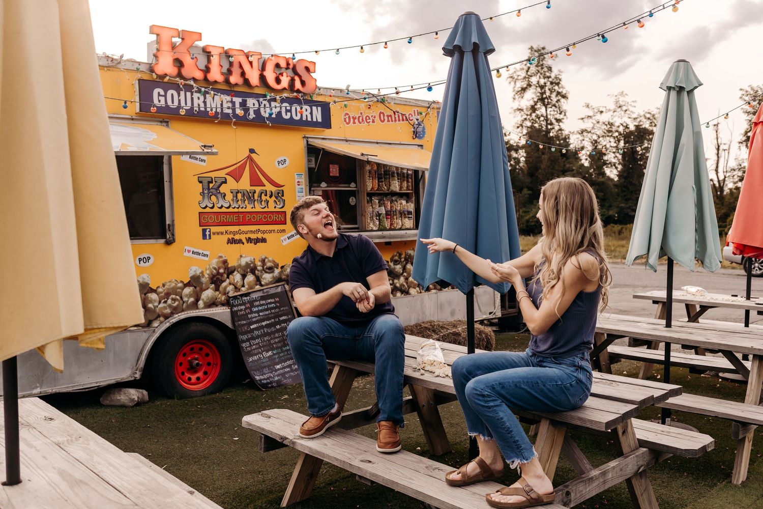 Couple chatting and sharing popcorn at a picnic table outside King's Gourmet Popcorn food truck.