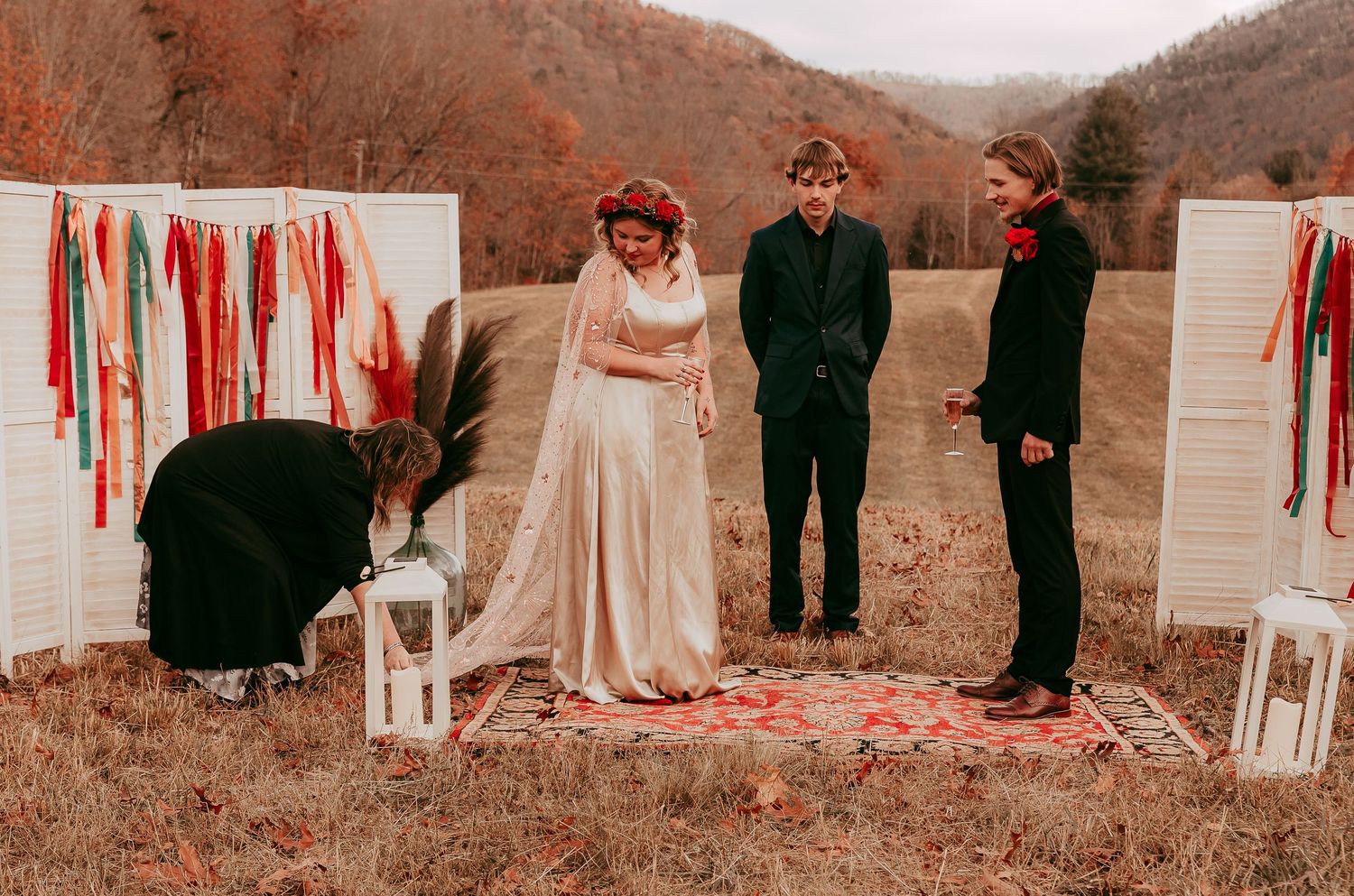 Bride and groom standing at outdoor fall wedding altar with white shutter backdrop and colorful ribbon streamers in mountains.