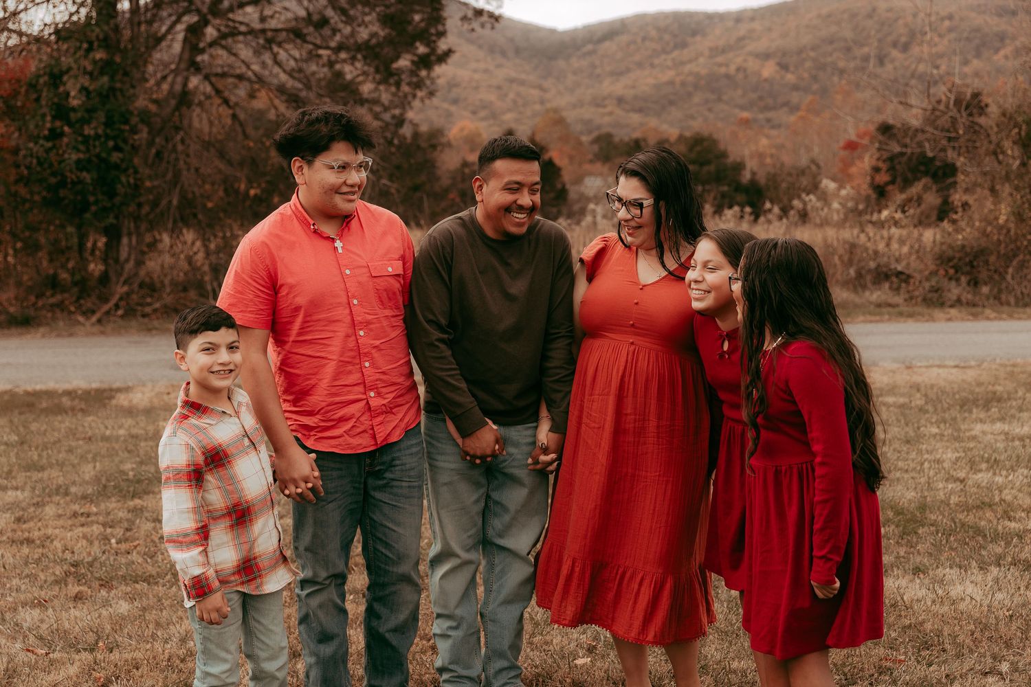 Joyful family of five laughing together in an open field during fall season.