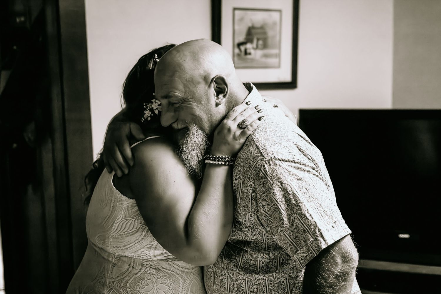 Black and white photo of an emotional bride and older man sharing a tender hug before the wedding.