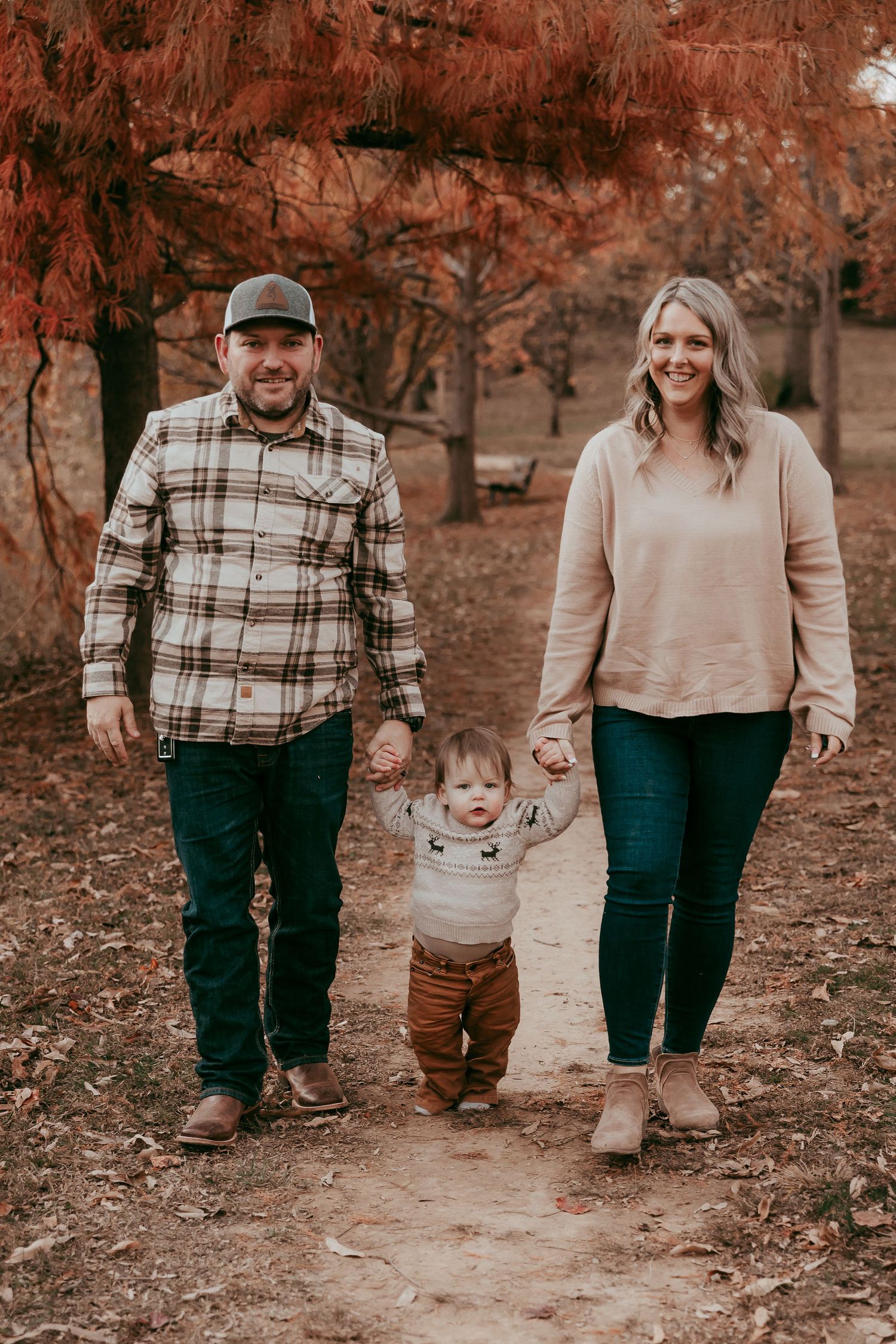 Happy couple walking with their toddler on a fall nature path lined with red trees.