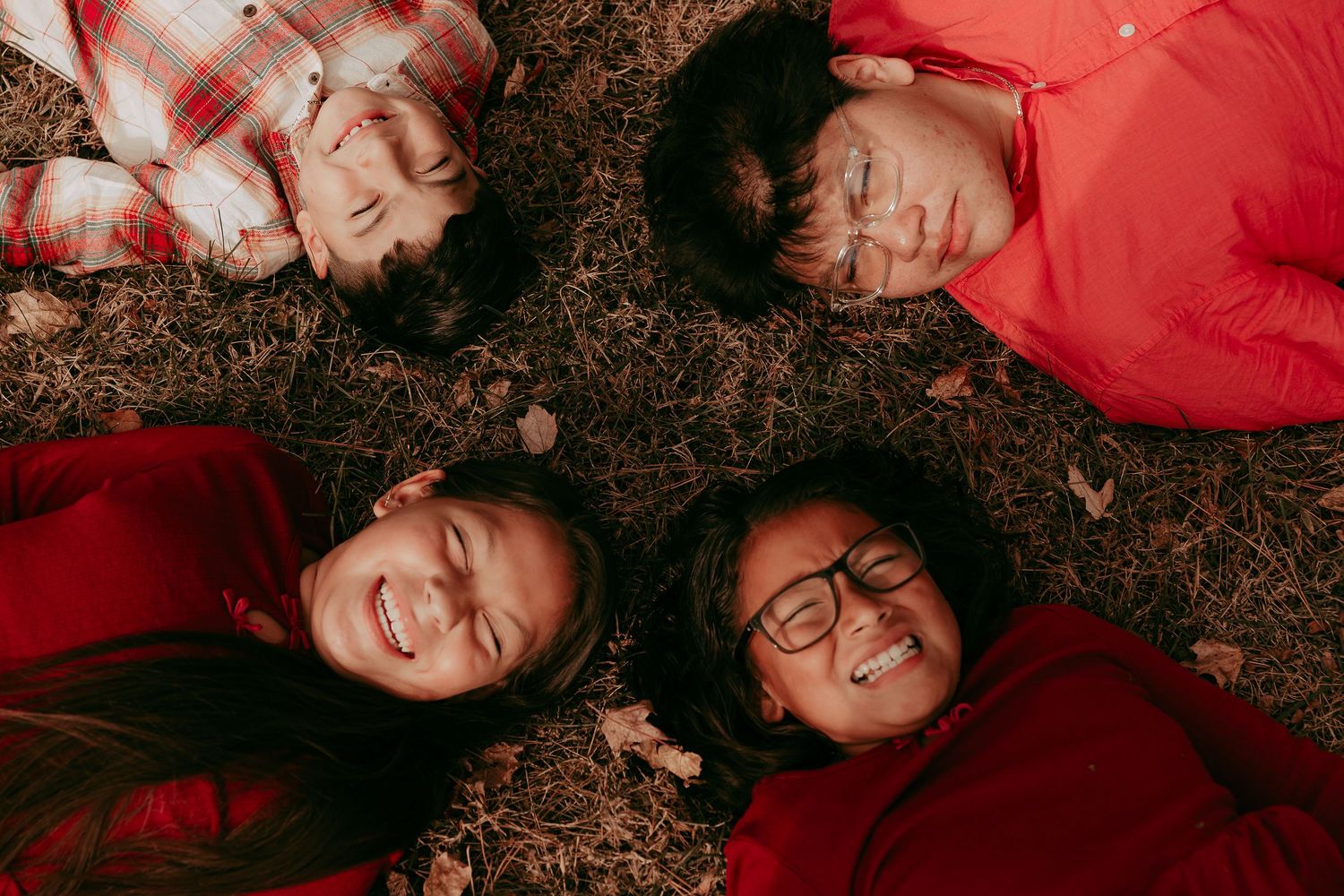 Four children lying in a circle on grass laughing during fall family photo session.