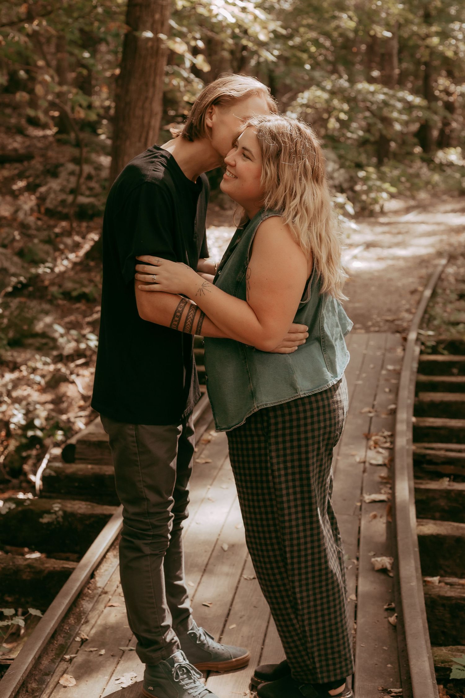 Couple embracing and kissing on rustic forest railway tracks surrounded by autumn trees.