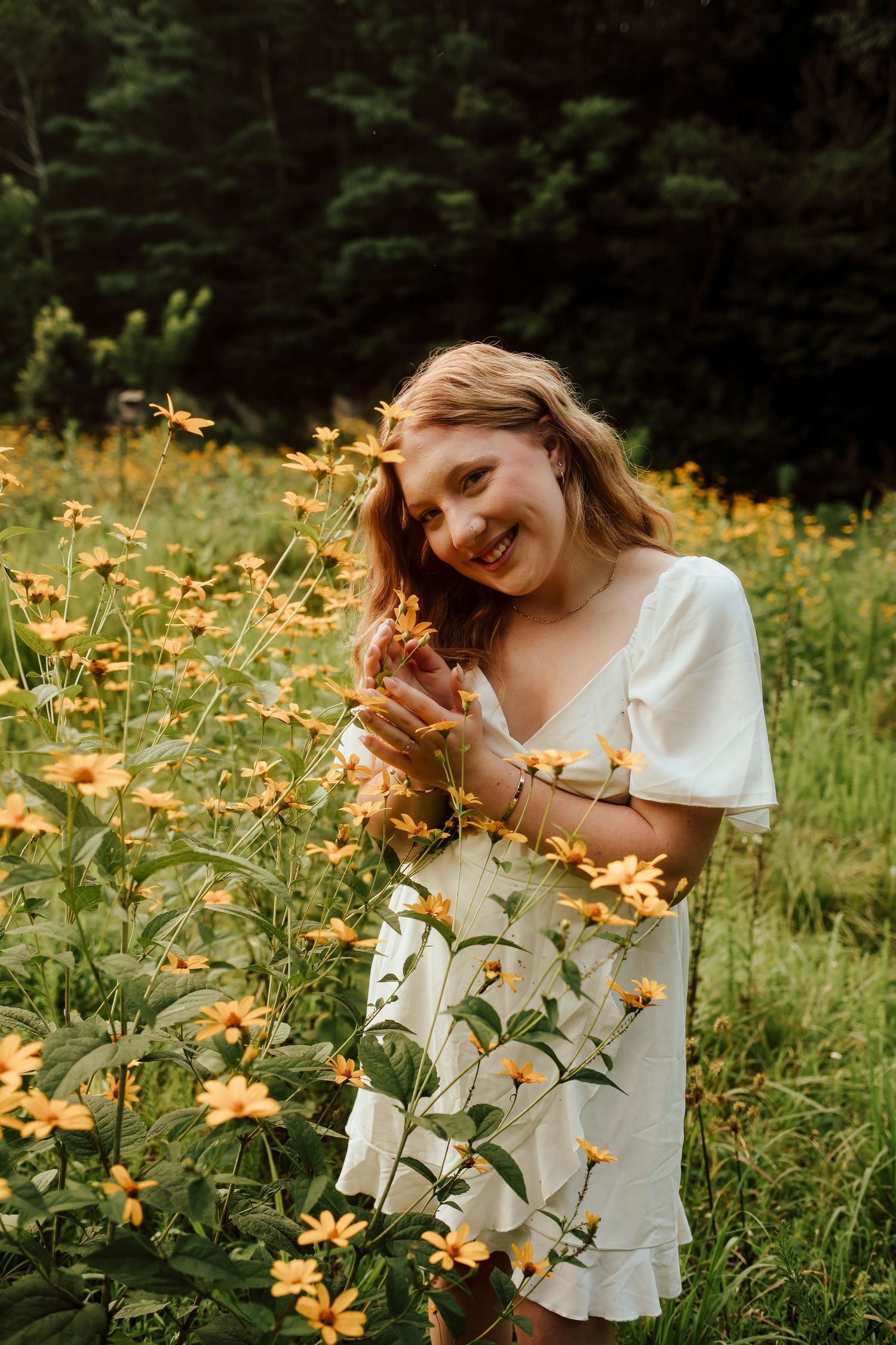 Young woman in white dress smiling among vibrant yellow wildflowers in a lush green meadow.