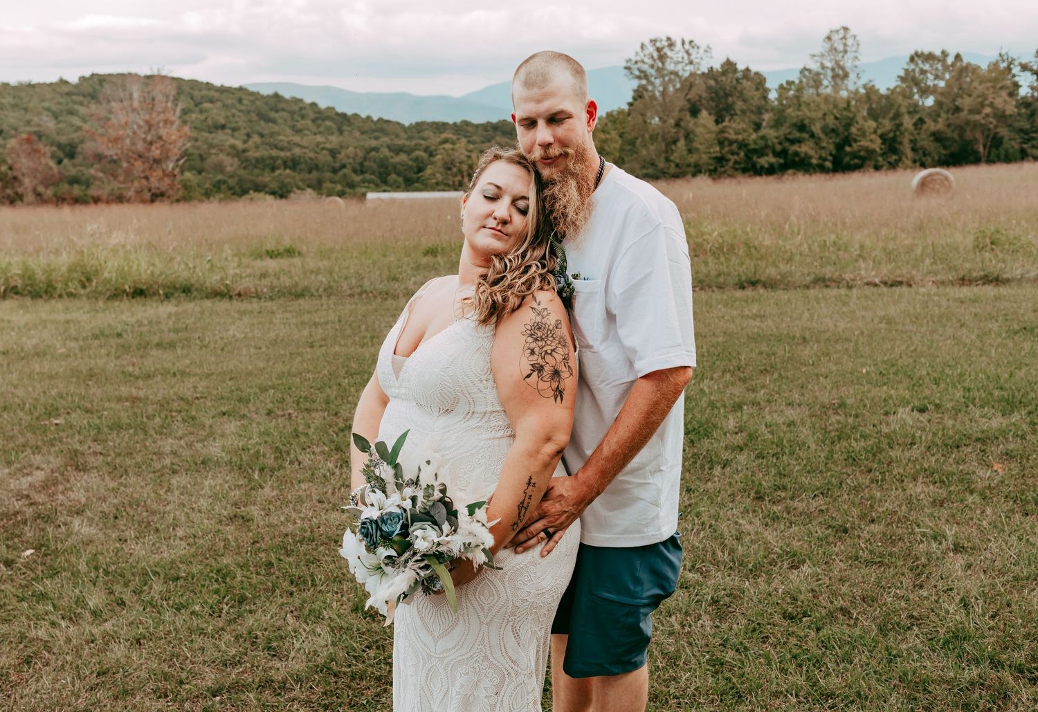 Bride and groom pose together in a mountain meadow, bride holding a white and blue wedding bouquet.