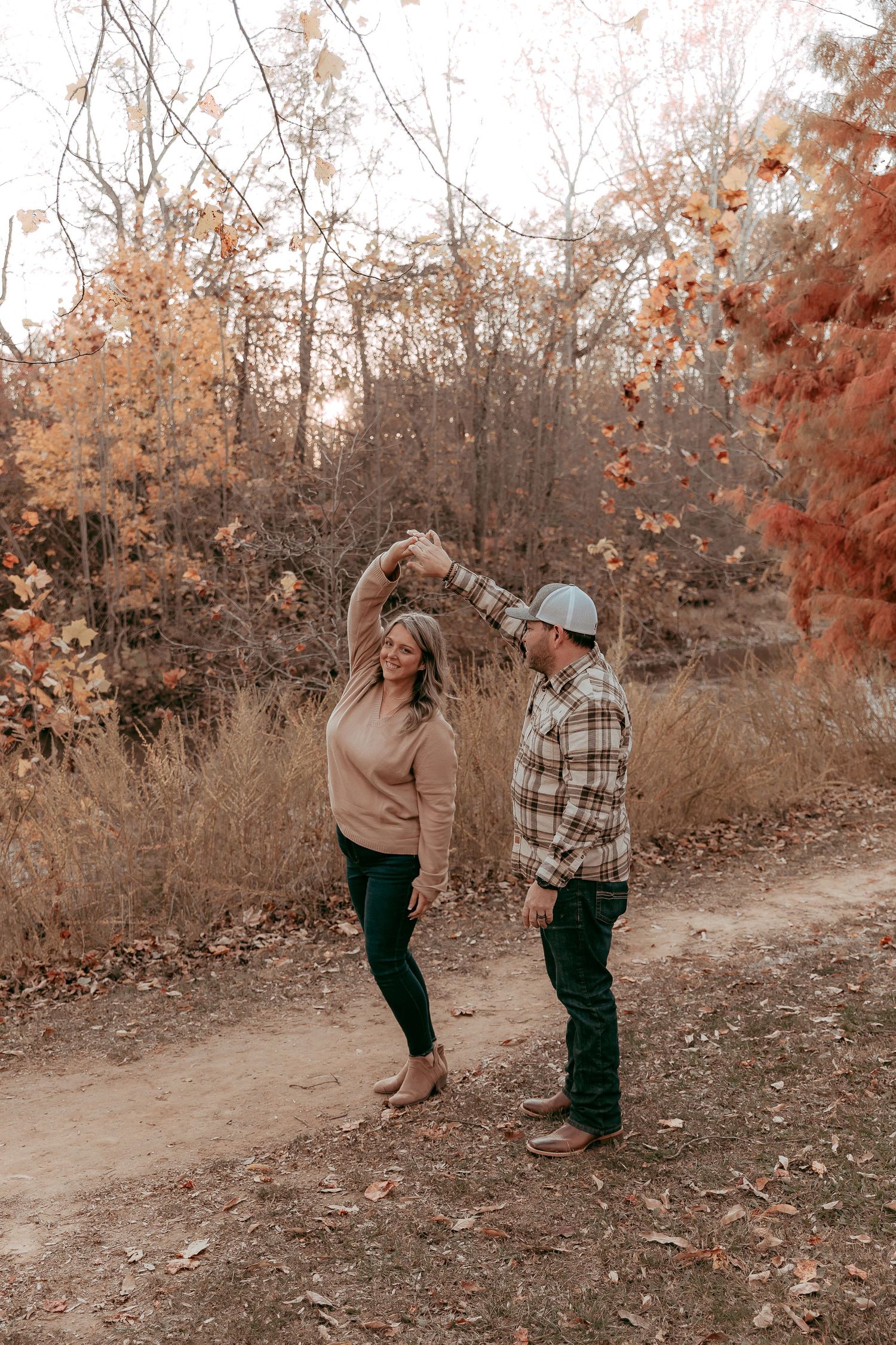 Couple dancing together on a scenic autumn trail surrounded by colorful fall foliage.