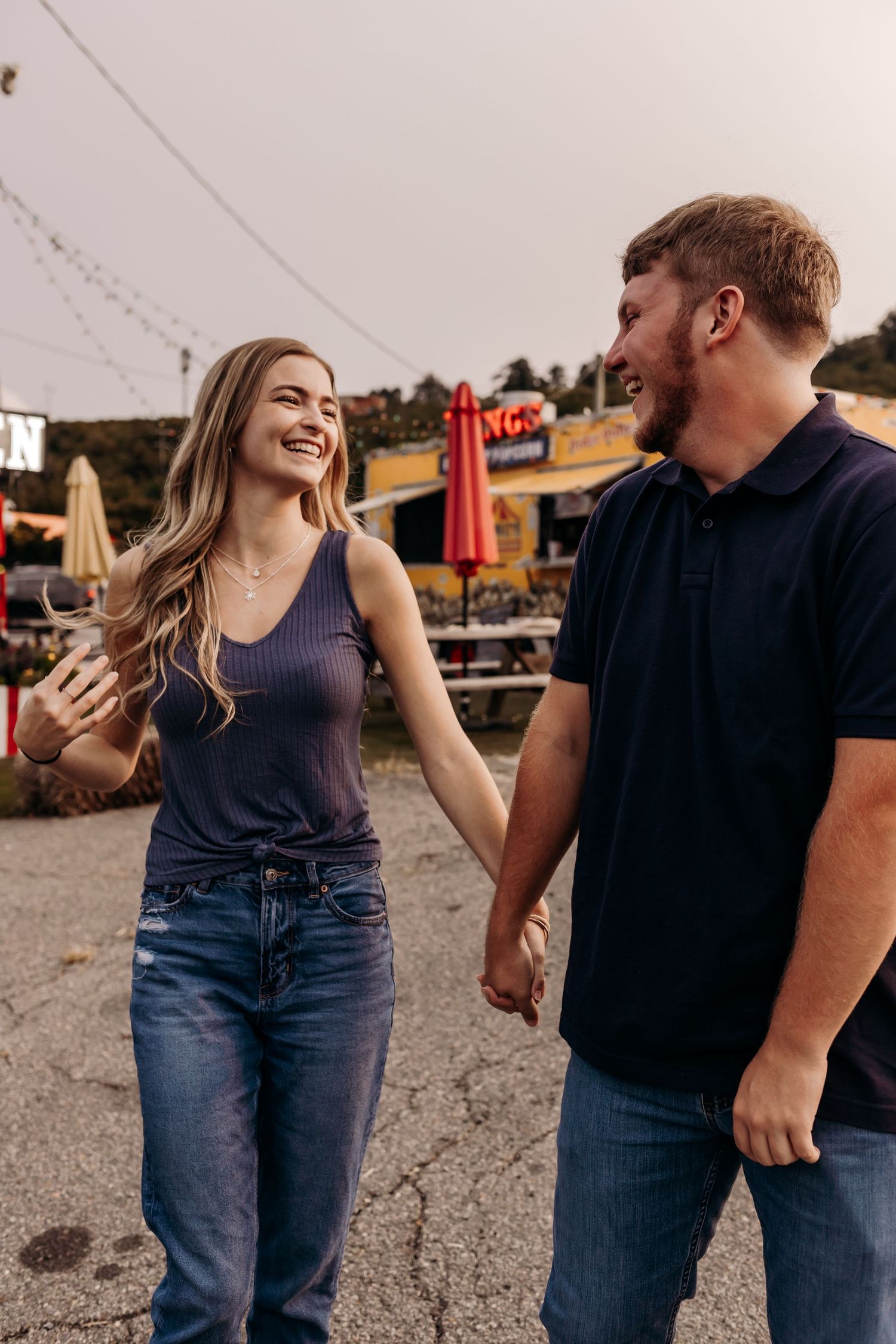 Happy couple holding hands and laughing together at an outdoor market at dusk.