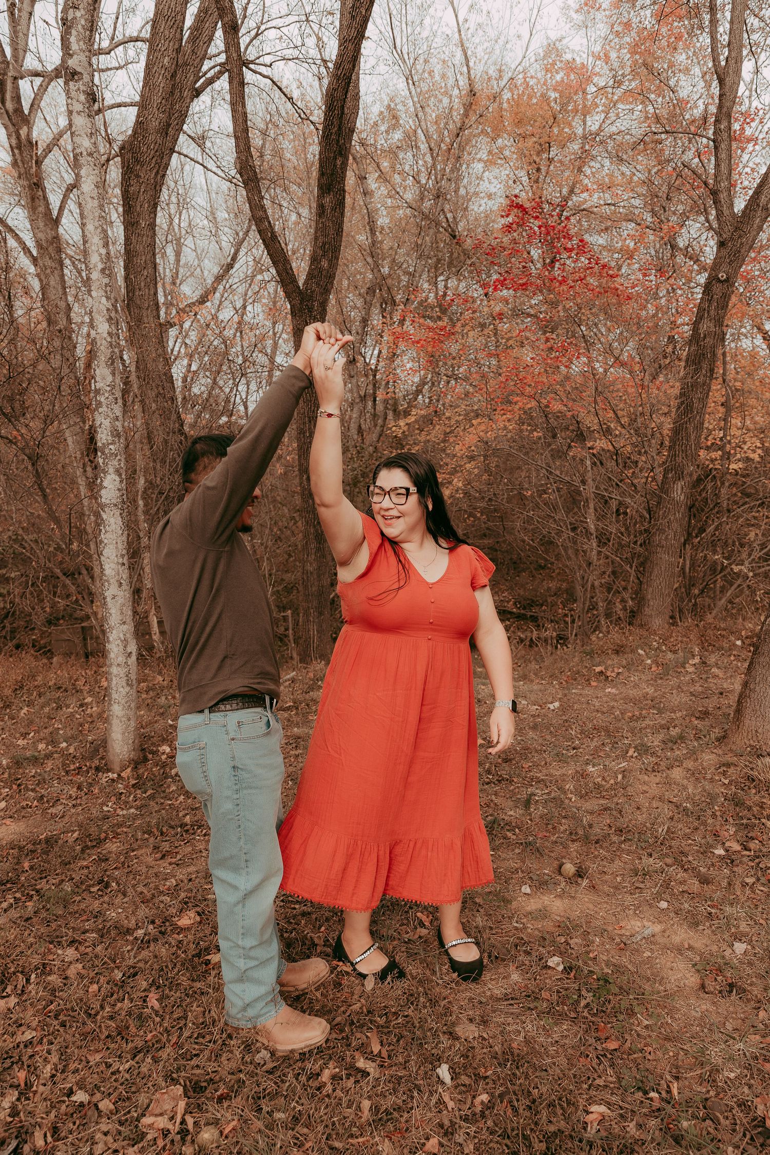 Couple dancing together among bare autumn trees in a wooded outdoor setting.