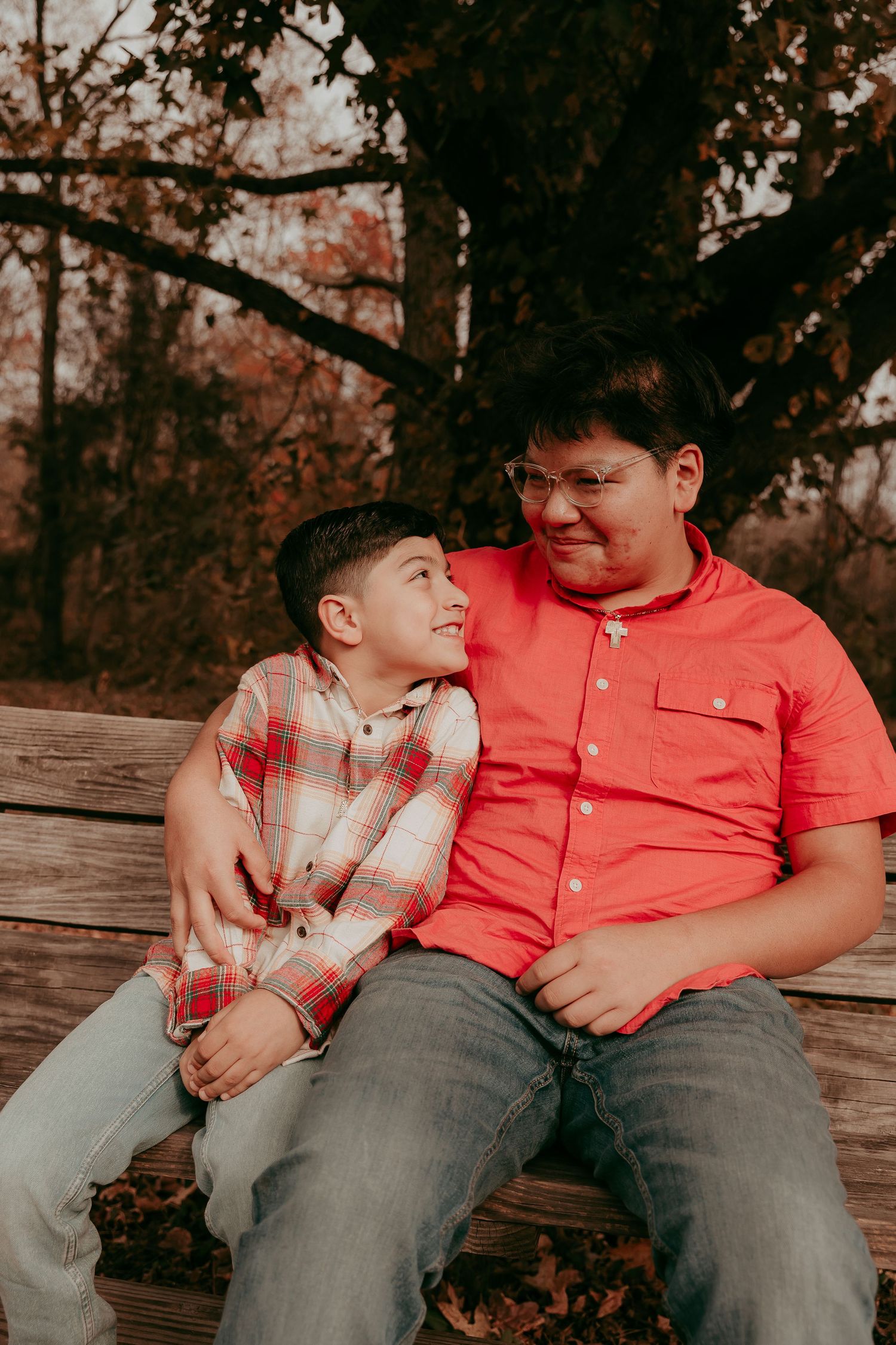Two brothers sharing a warm moment on a wooden bench in autumn setting.
