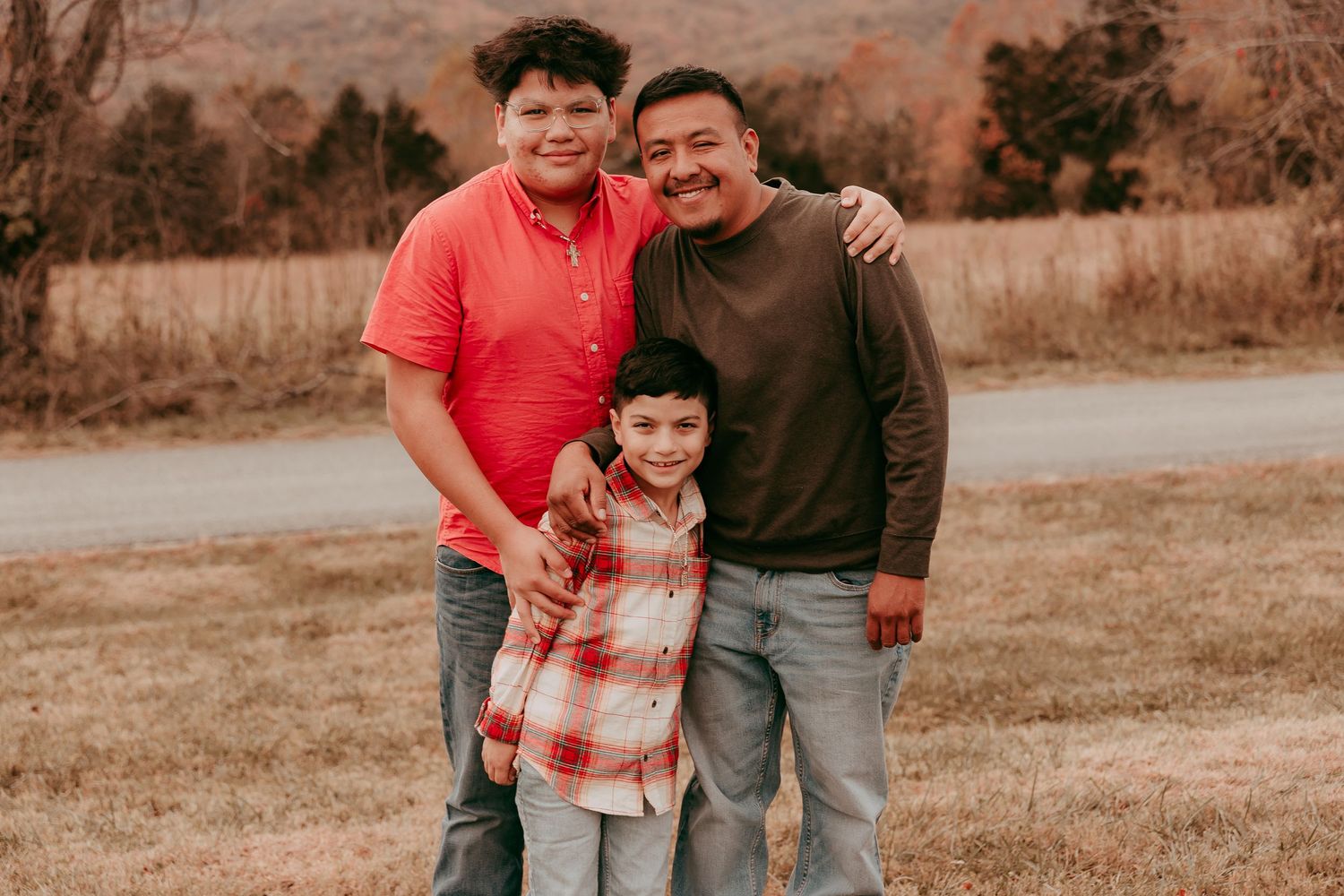 Family of three smiling outdoors in fall, two boys and a young girl in a plaid shirt posing in a field.