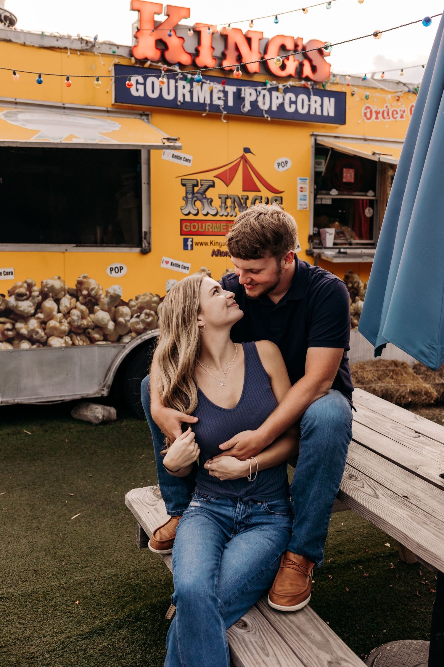 Couple sharing a romantic moment at a picnic bench in front of King's Gourmet Popcorn food truck.