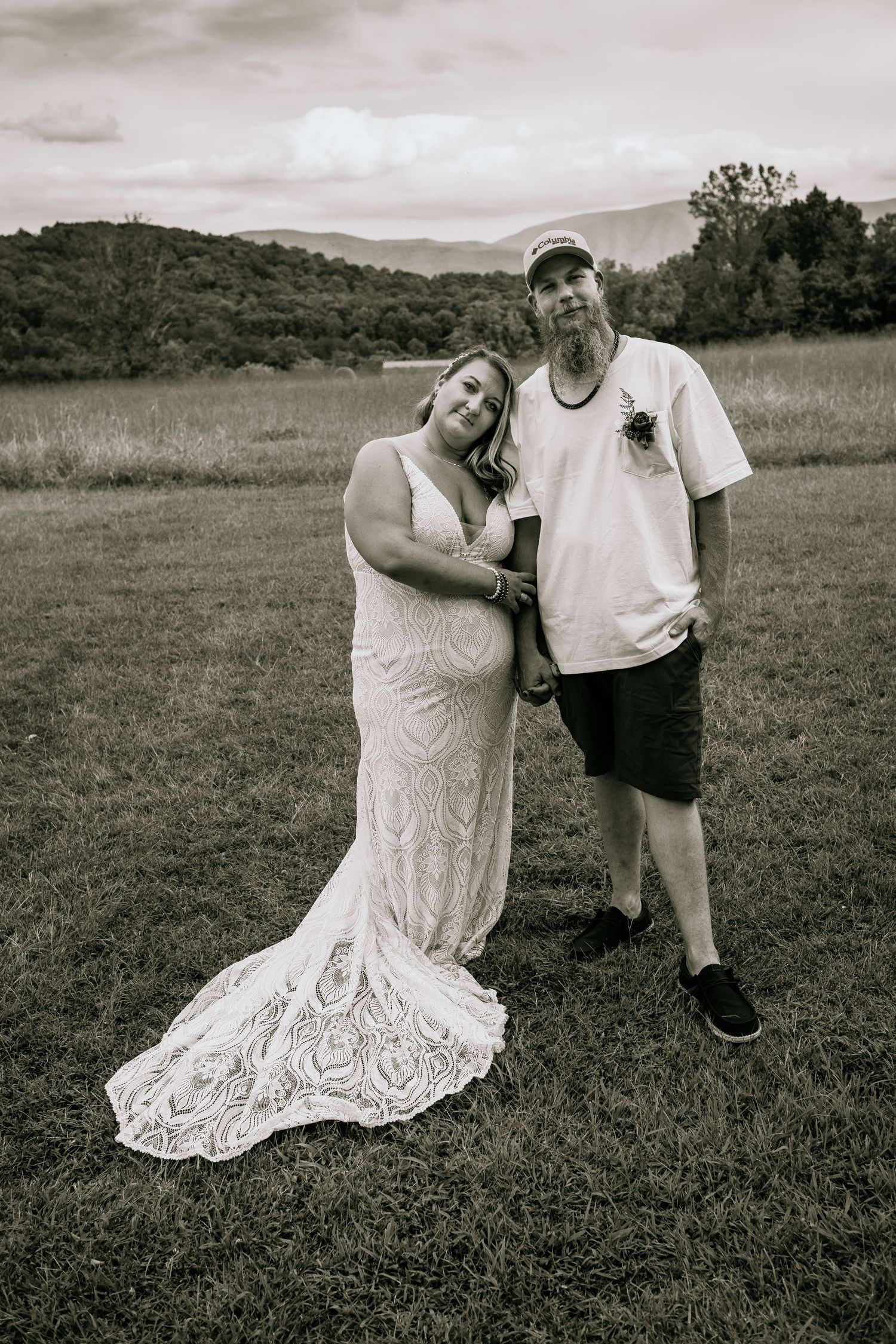 Black and white portrait of bride and groom posing together in a rustic mountain field wedding setting.