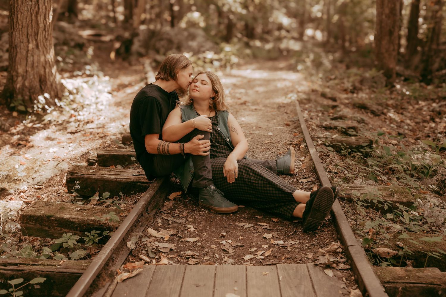 Romantic couple cuddling on wooden forest railway tracks among fallen autumn leaves.