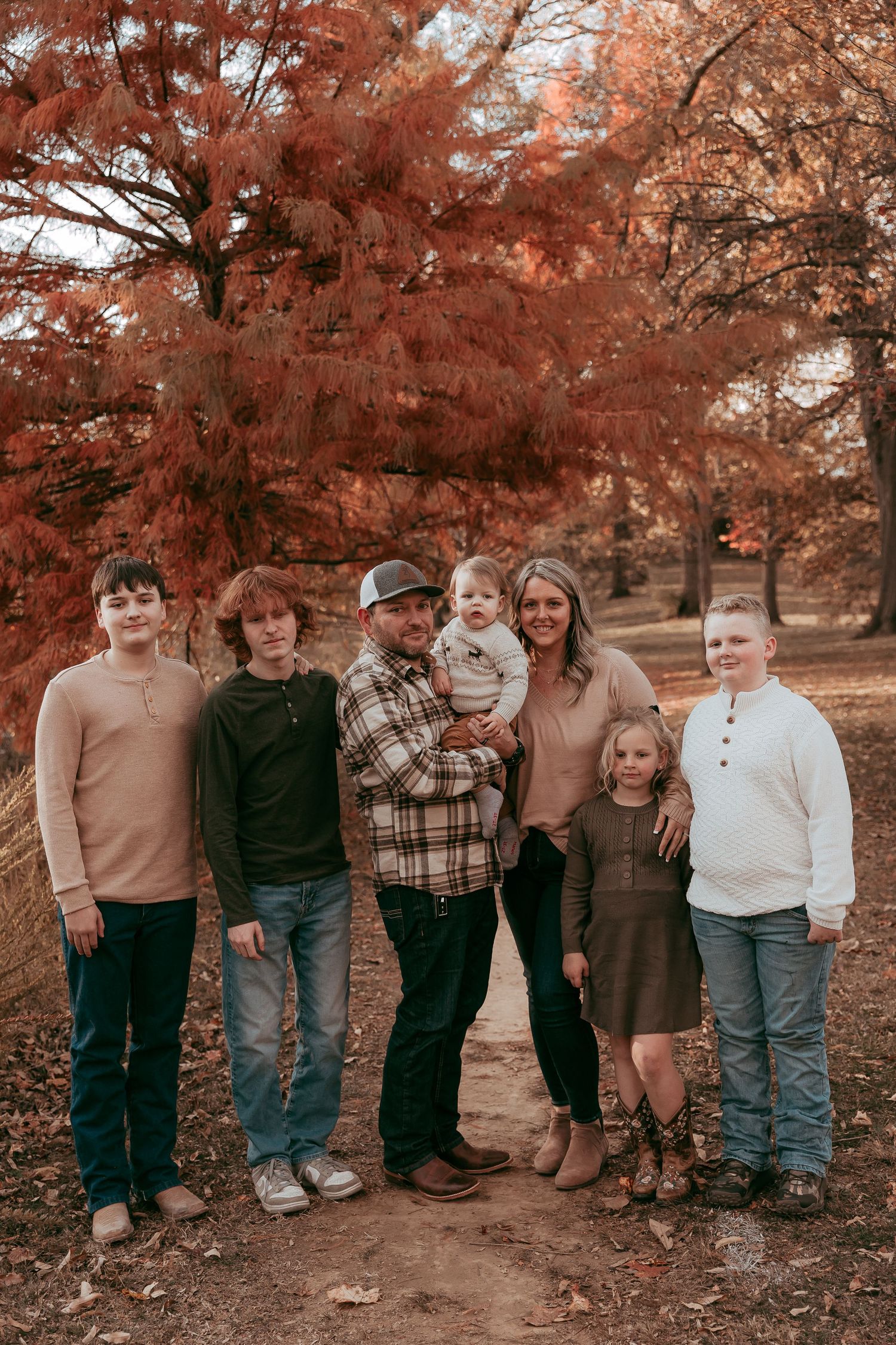Family of seven poses together under vibrant red autumn trees on a scenic park path.