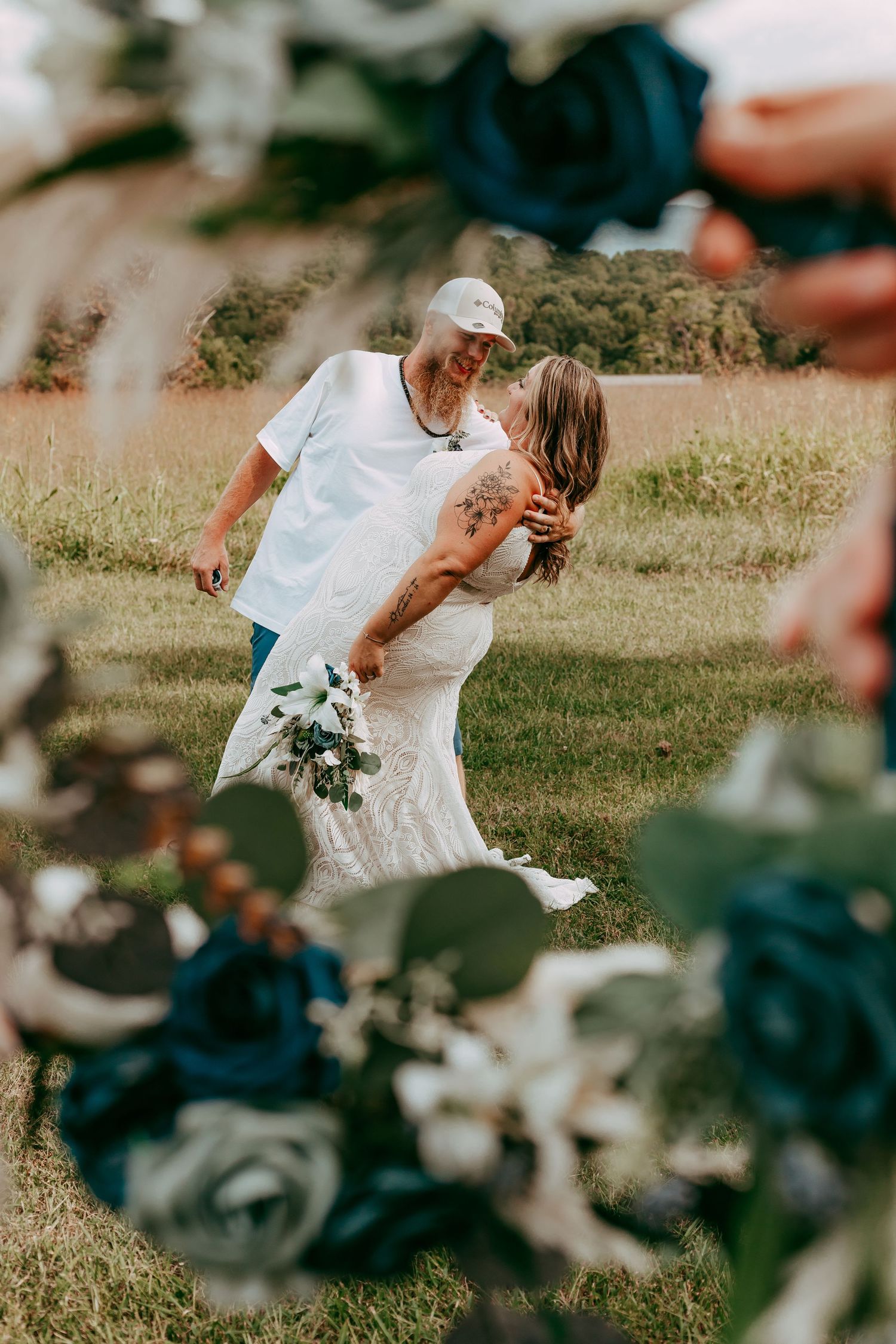 Bride and groom share a tender kiss framed by blue and white floral wedding decorations in a field.