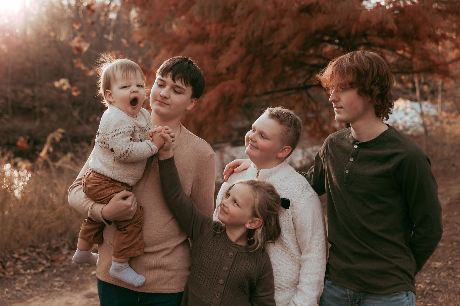 Family of five posing together outdoors surrounded by vibrant red fall foliage.