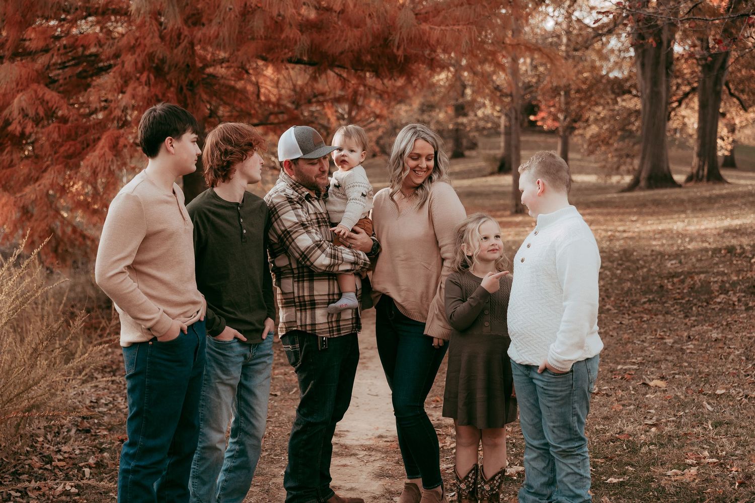 Family laughs and chats together on a tree-lined path surrounded by red autumn foliage.
