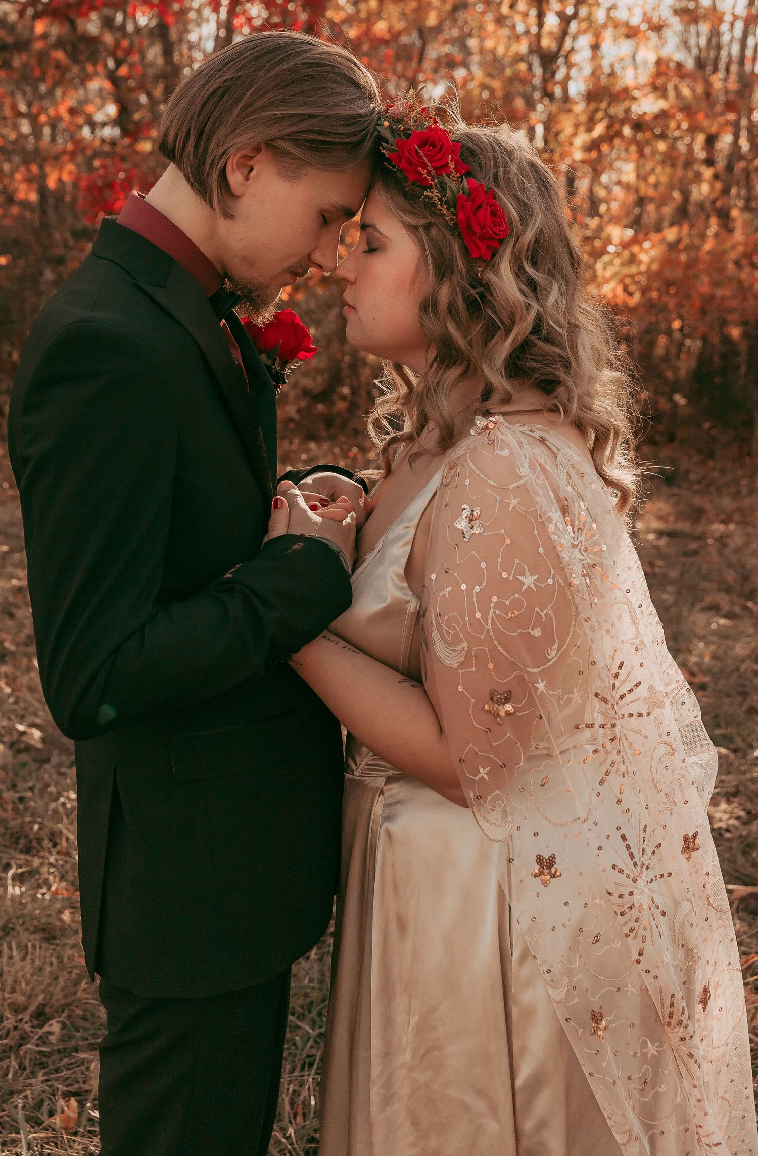 Bride and groom share romantic moment forehead-to-forehead in autumn woodland setting.
