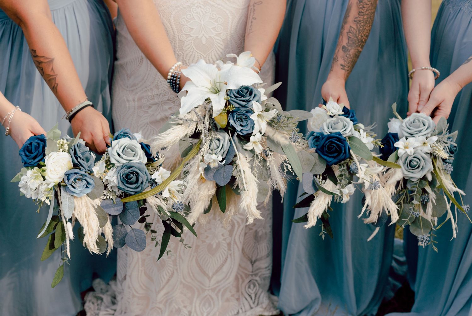 Bride and bridesmaids holding stunning blue and white rose bouquets with feathers at an outdoor wedding.