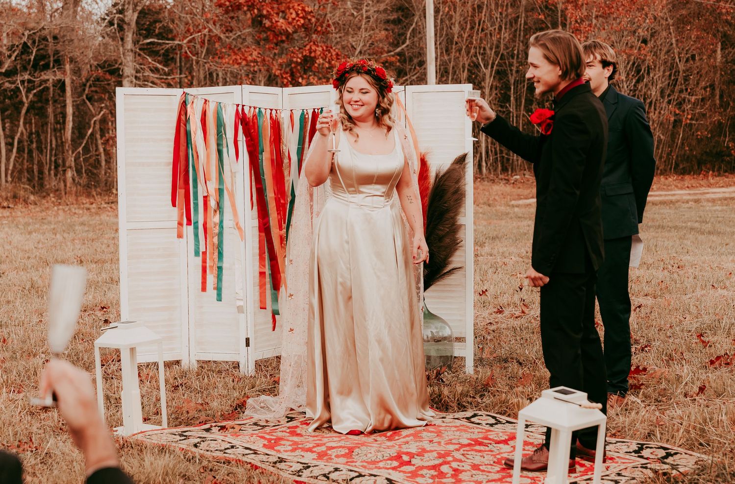 Joyful bride in champagne gown laughing with groom at outdoor fall wedding ceremony with colorful ribbon backdrop.