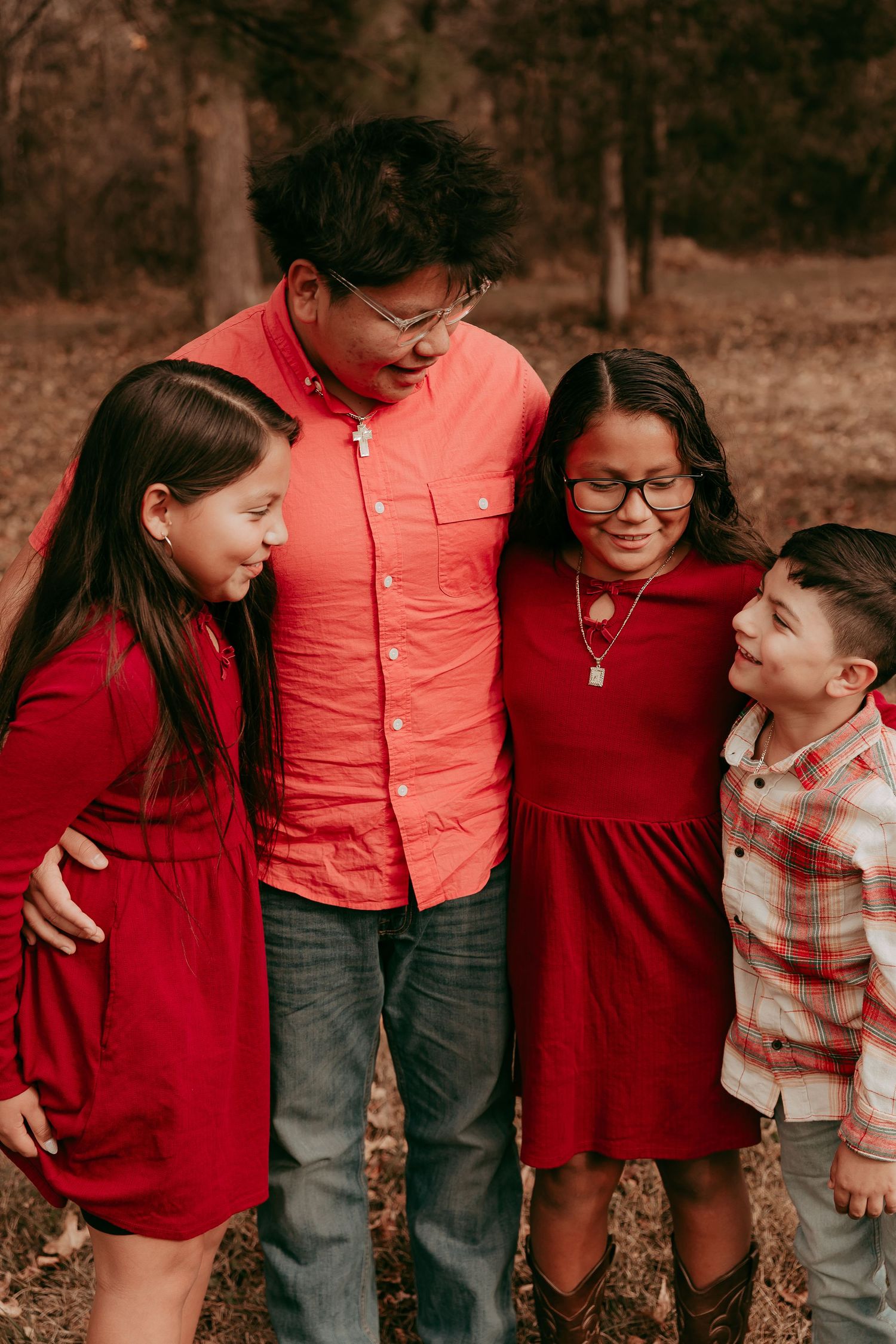 Four siblings sharing a warm embrace while wearing coordinating red outfits in fall.