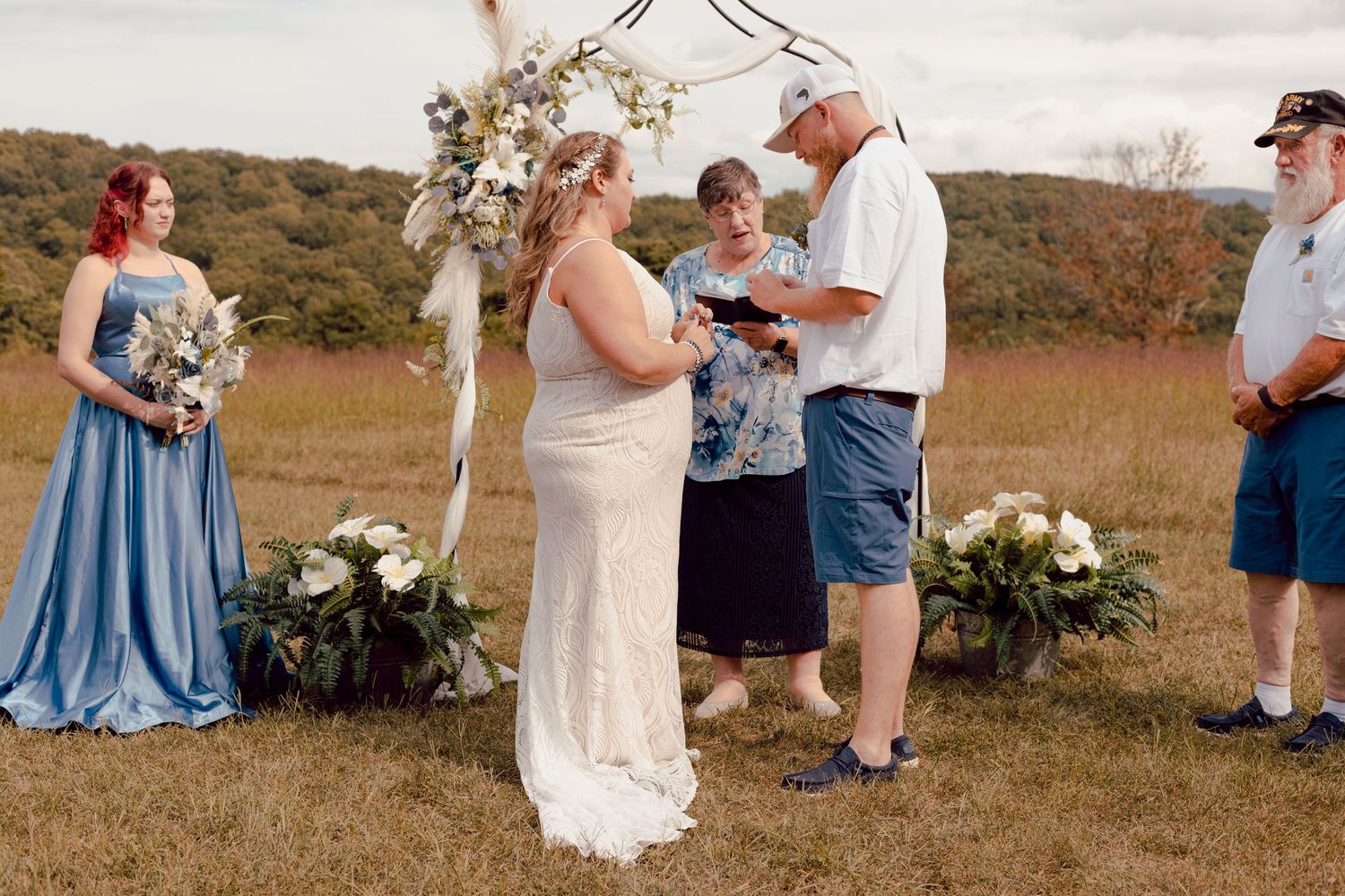 Bride and groom exchanging rings at an outdoor rustic wedding ceremony with a boho floral arch.
