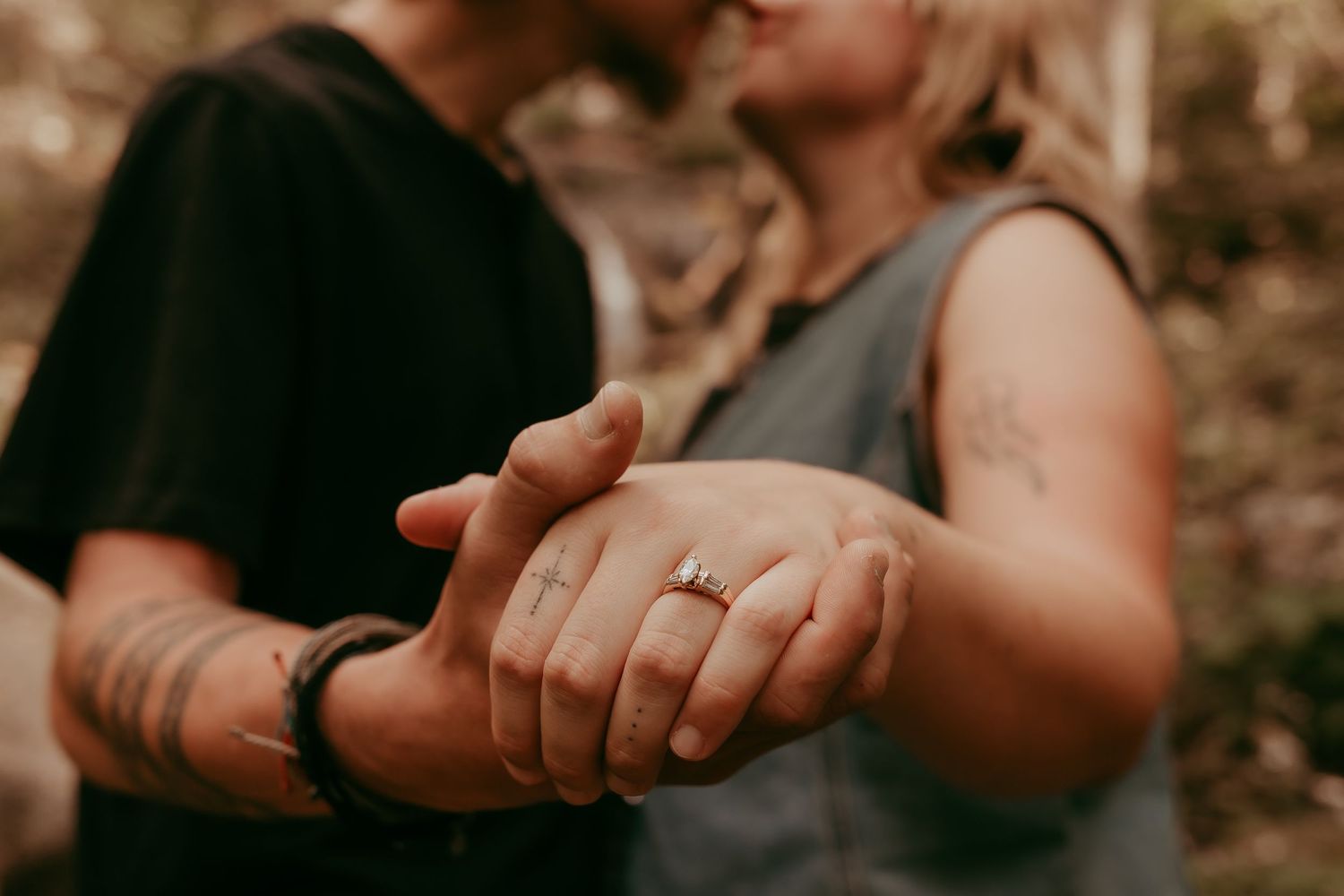 Close-up of couple holding hands displaying engagement ring with tattoos visible.