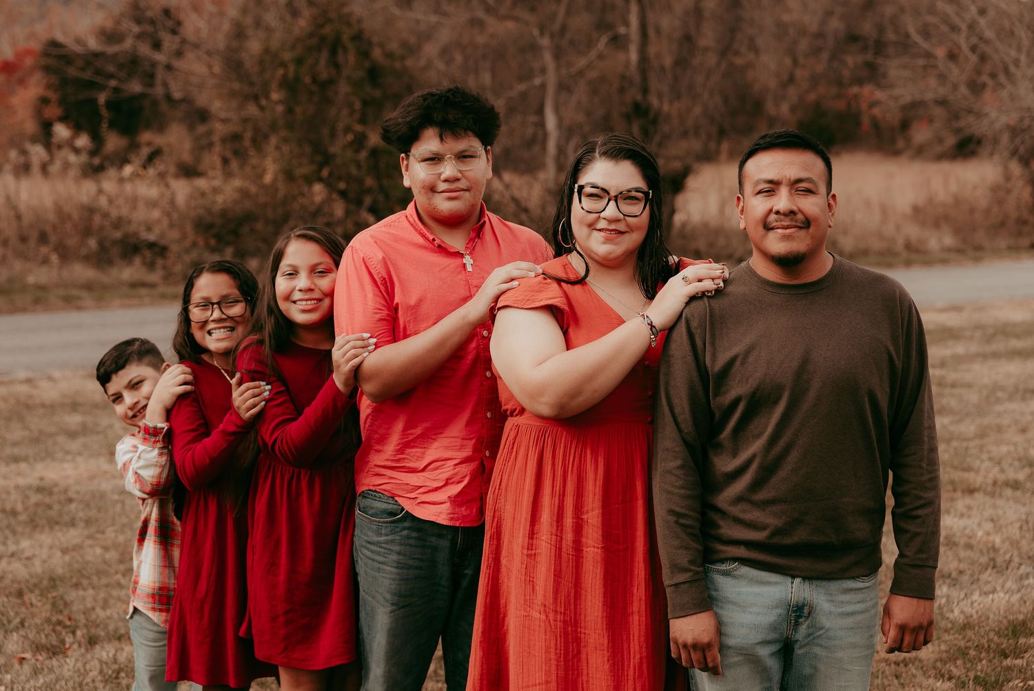Family of six posing playfully in a row in a scenic autumn outdoor setting.