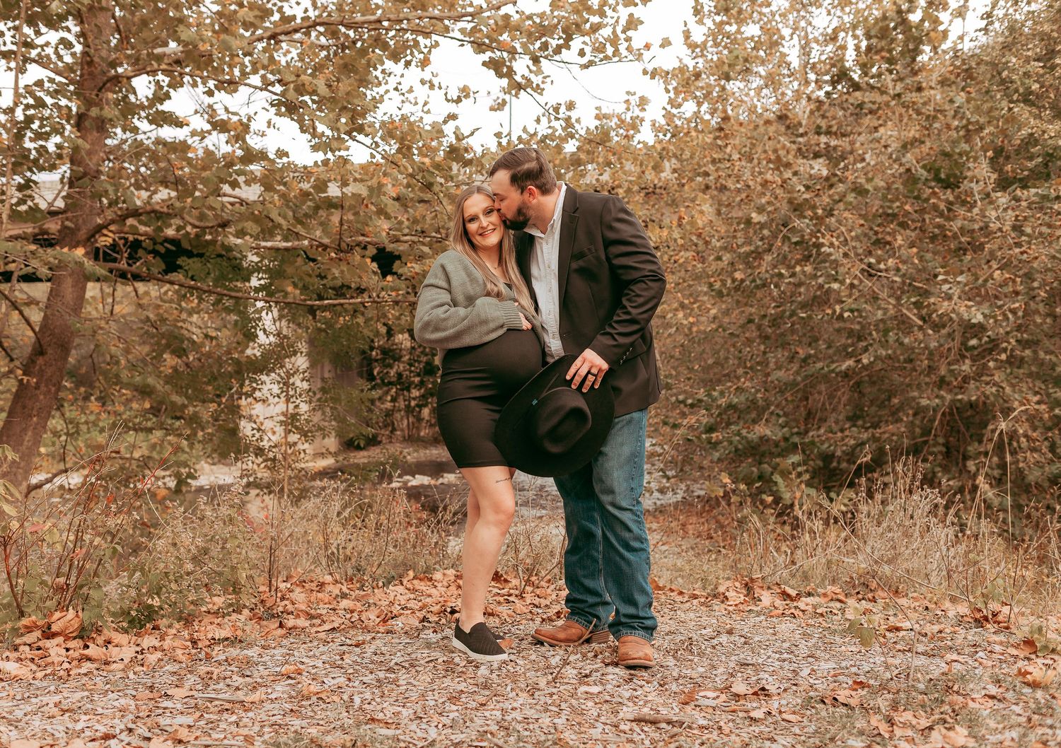 Pregnant woman in green sweater and man sharing a joyful moment in autumn park.