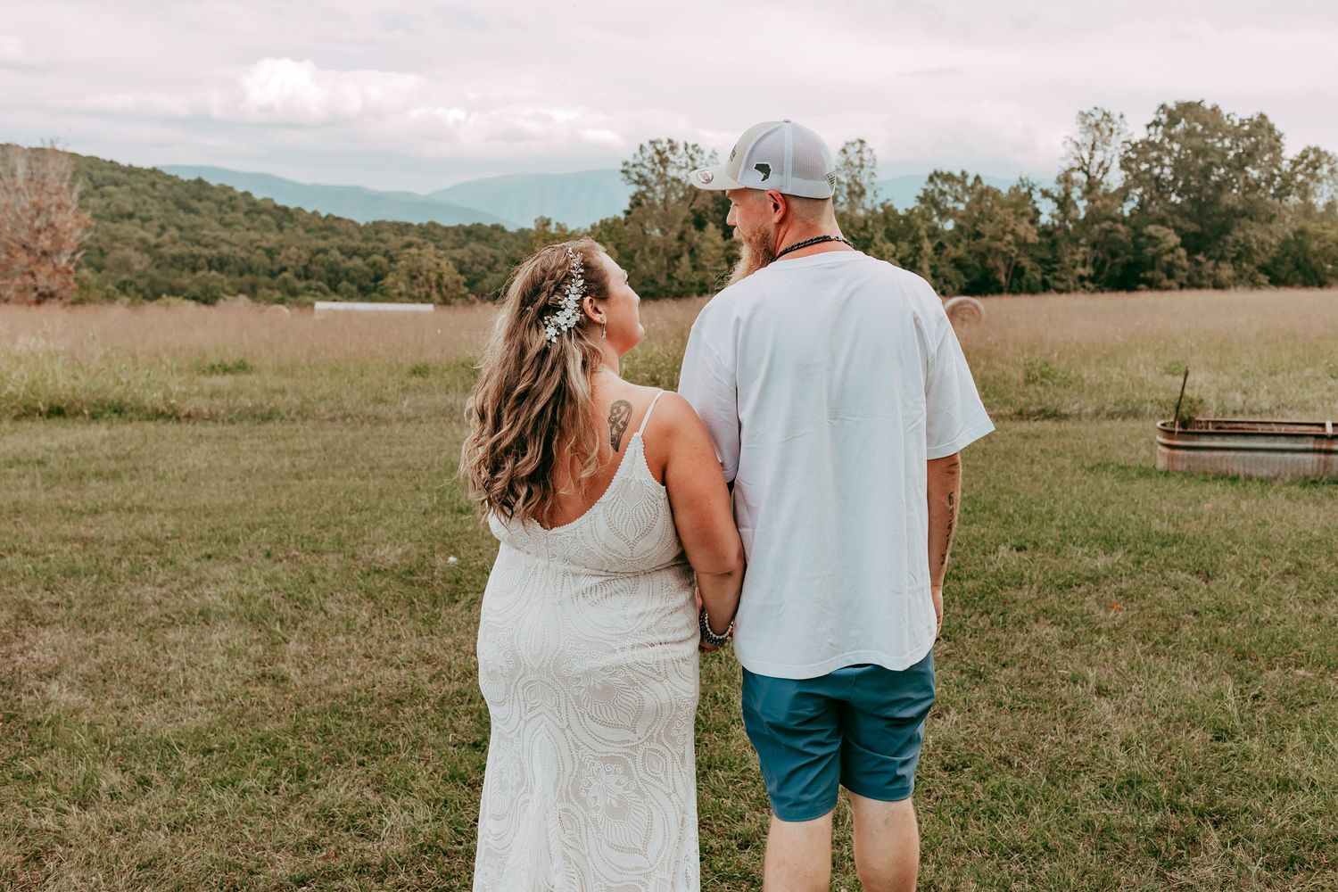 Bride and groom walk hand in hand through a scenic mountain meadow at their outdoor wedding.