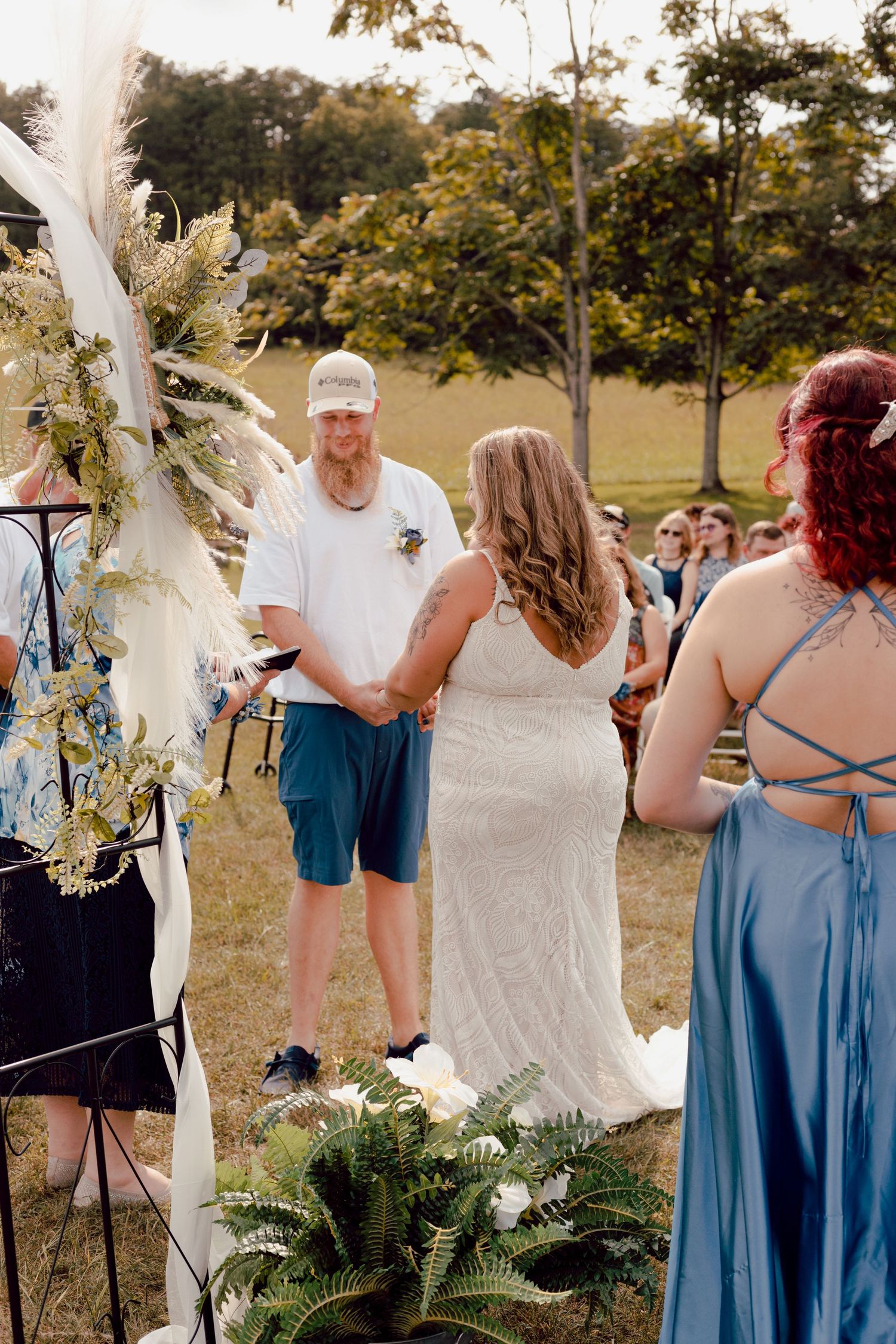 Outdoor rustic wedding ceremony with bride and groom exchanging vows at a boho floral arch.