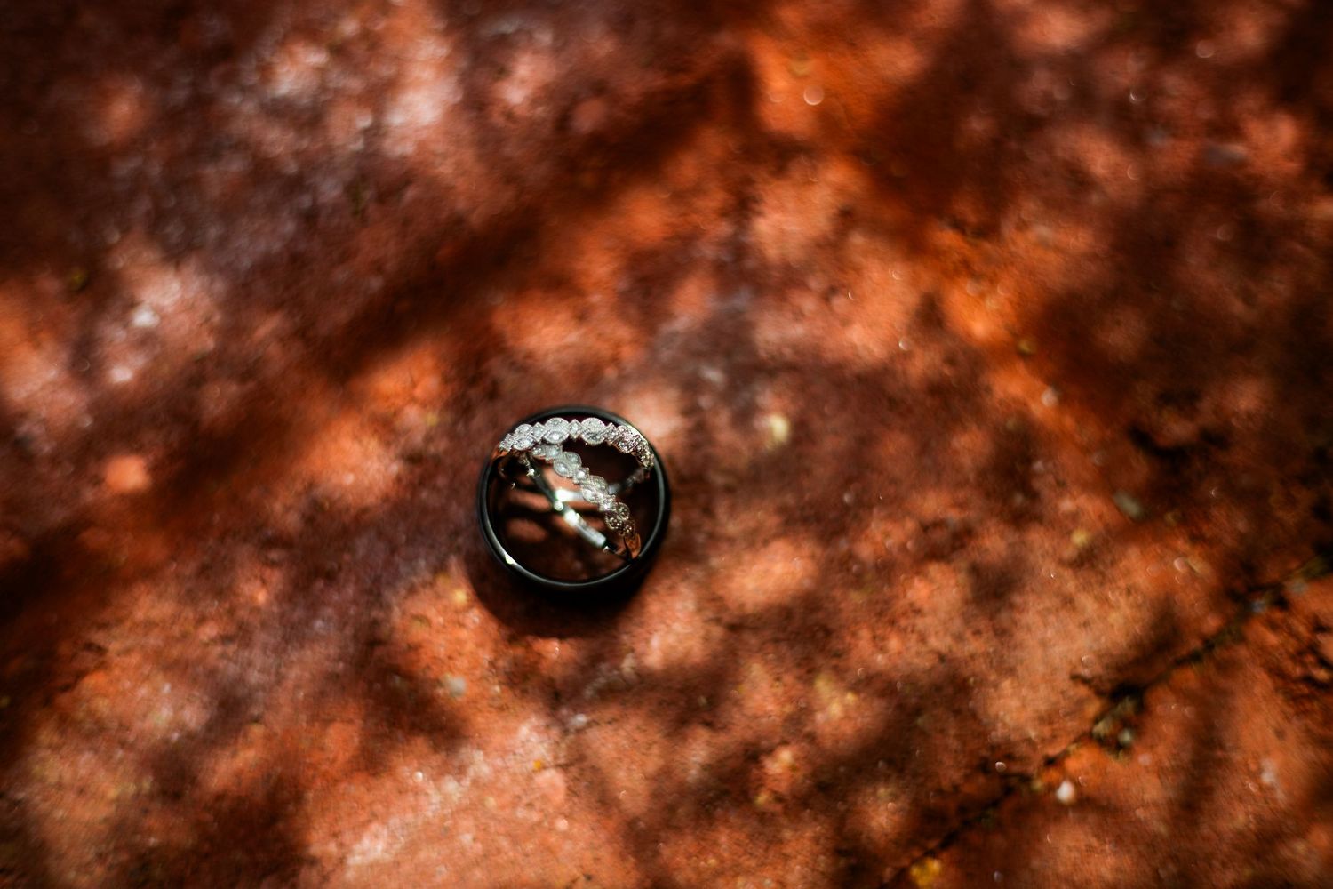 Close-up of diamond engagement ring resting on rustic brown textured surface with dappled light shadows.