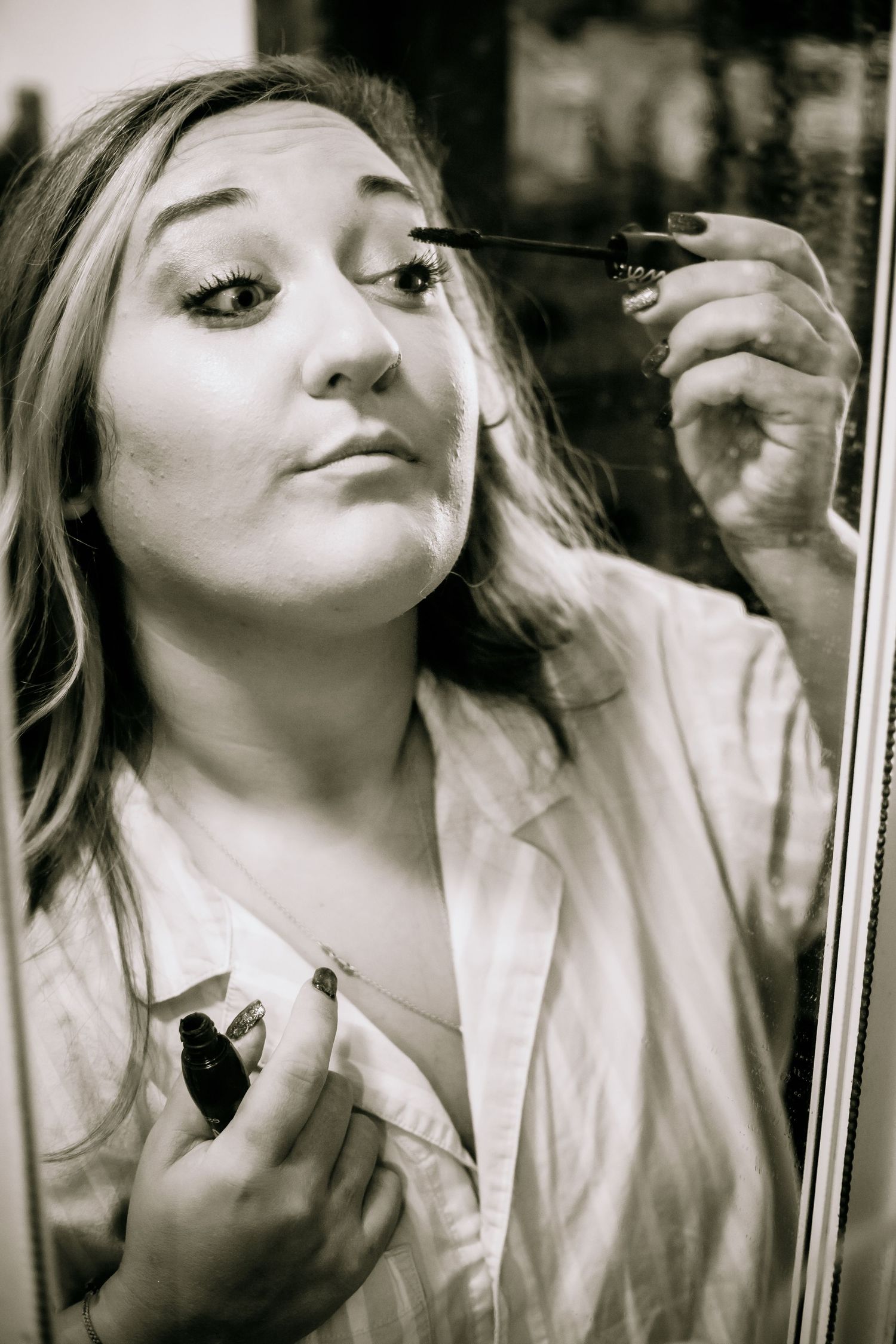 Black and white photo of a blonde bride applying mascara while getting ready for her wedding.