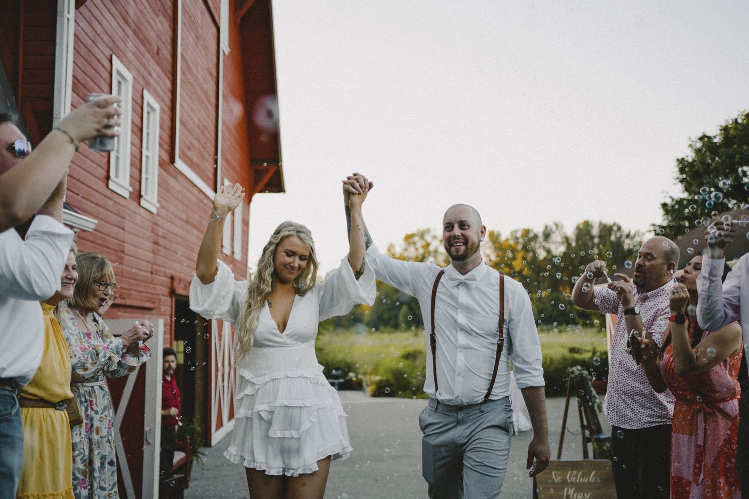 Celebratory bubble exit with couple holding hands walking past cheering guests blowing bubbles, cinematic documentary wedding photography