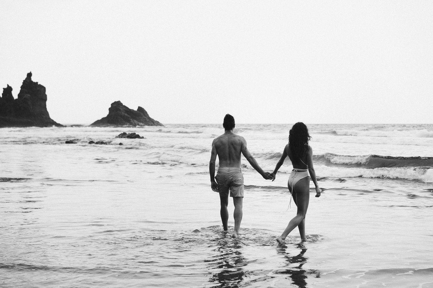 Black and white film beach silhouette of couple holding hands in Tenerife, Spain, destination engagement photography with ocean backdrop