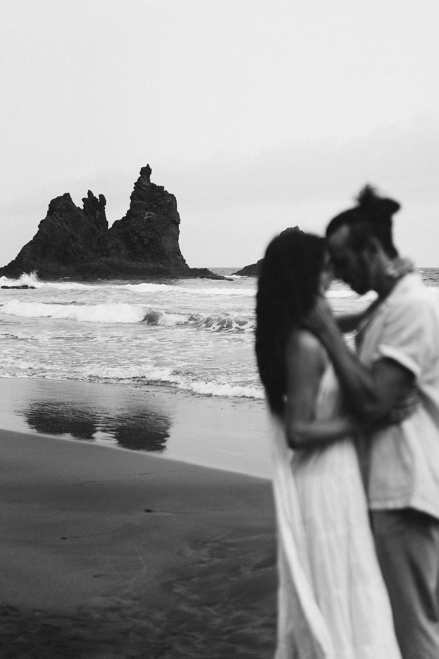 Black and white 35mm film beach portrait in Tenerife with rocky coastline, destination engagement photography with minimalist composition