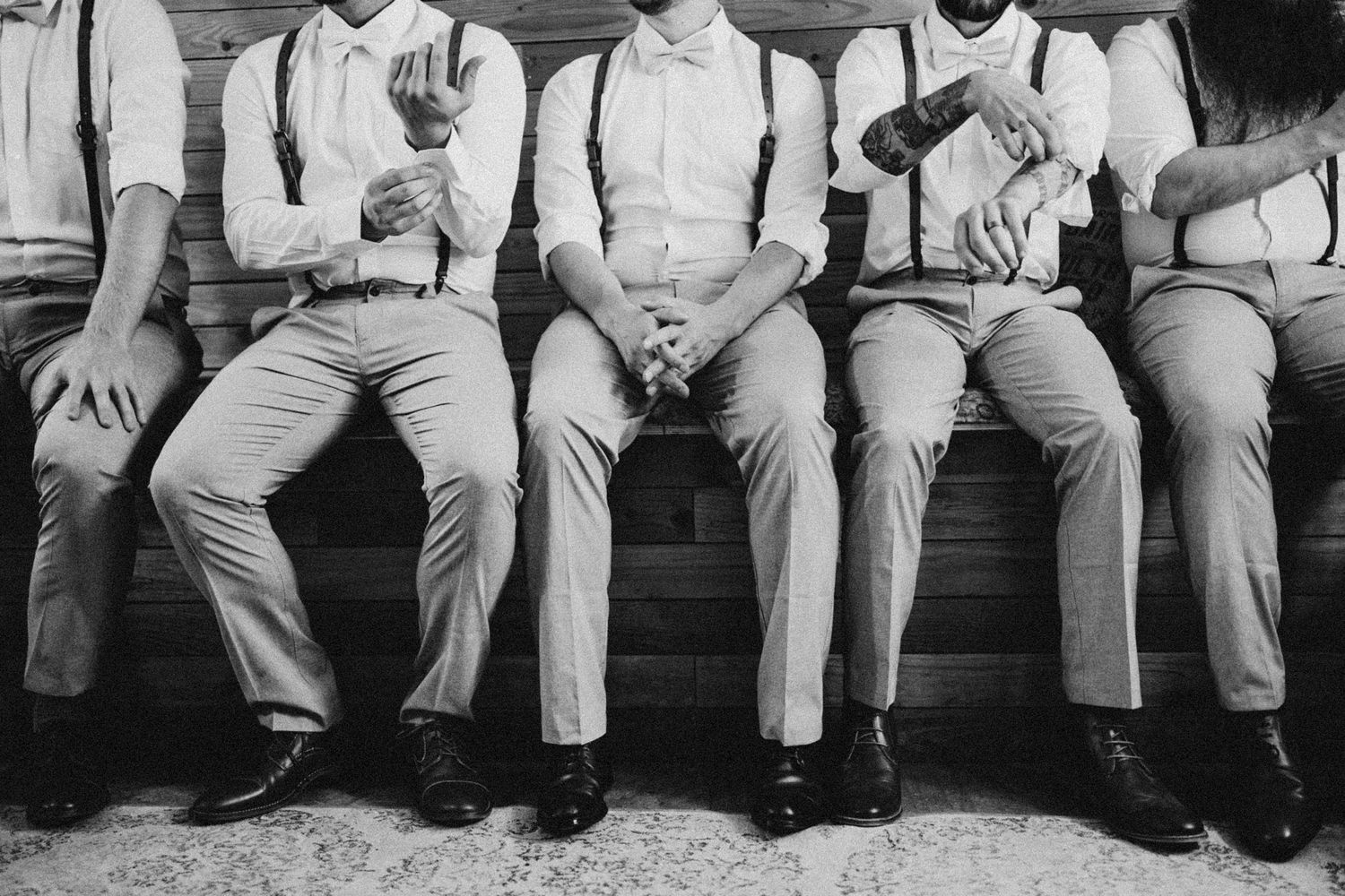 Black and white 35mm film groomsmen detail shot showing suits and formal attire, cinematic documentary style capturing wedding party
