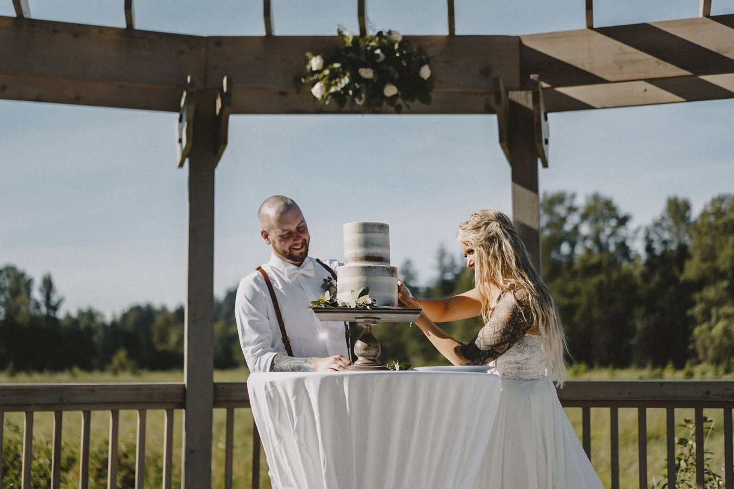 Couple cutting their wedding cake at outdoor Seattle venue with golden hour lighting and rustic wooden arch elements
