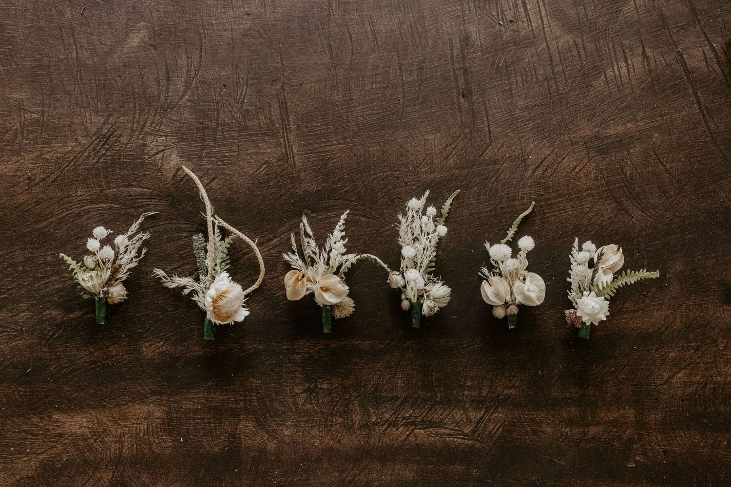 Elegant white floral boutonnières with delicate greenery for Tulum destination wedding, styled on dark wood showcasing refined details