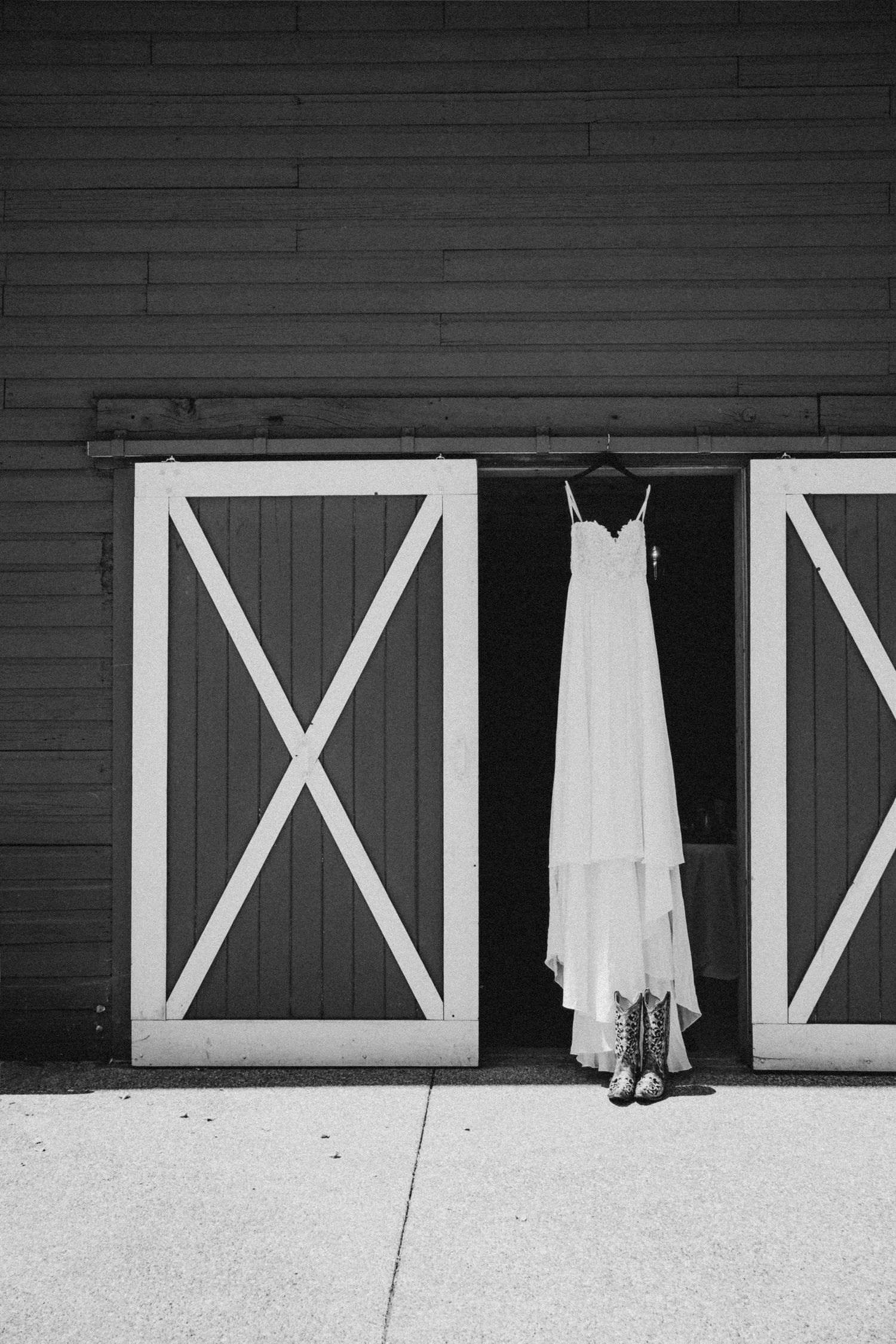 Black and white shot of dress hanging from barn doors, cinematic wedding photography showing dress silhouette against rustic Seattle venue