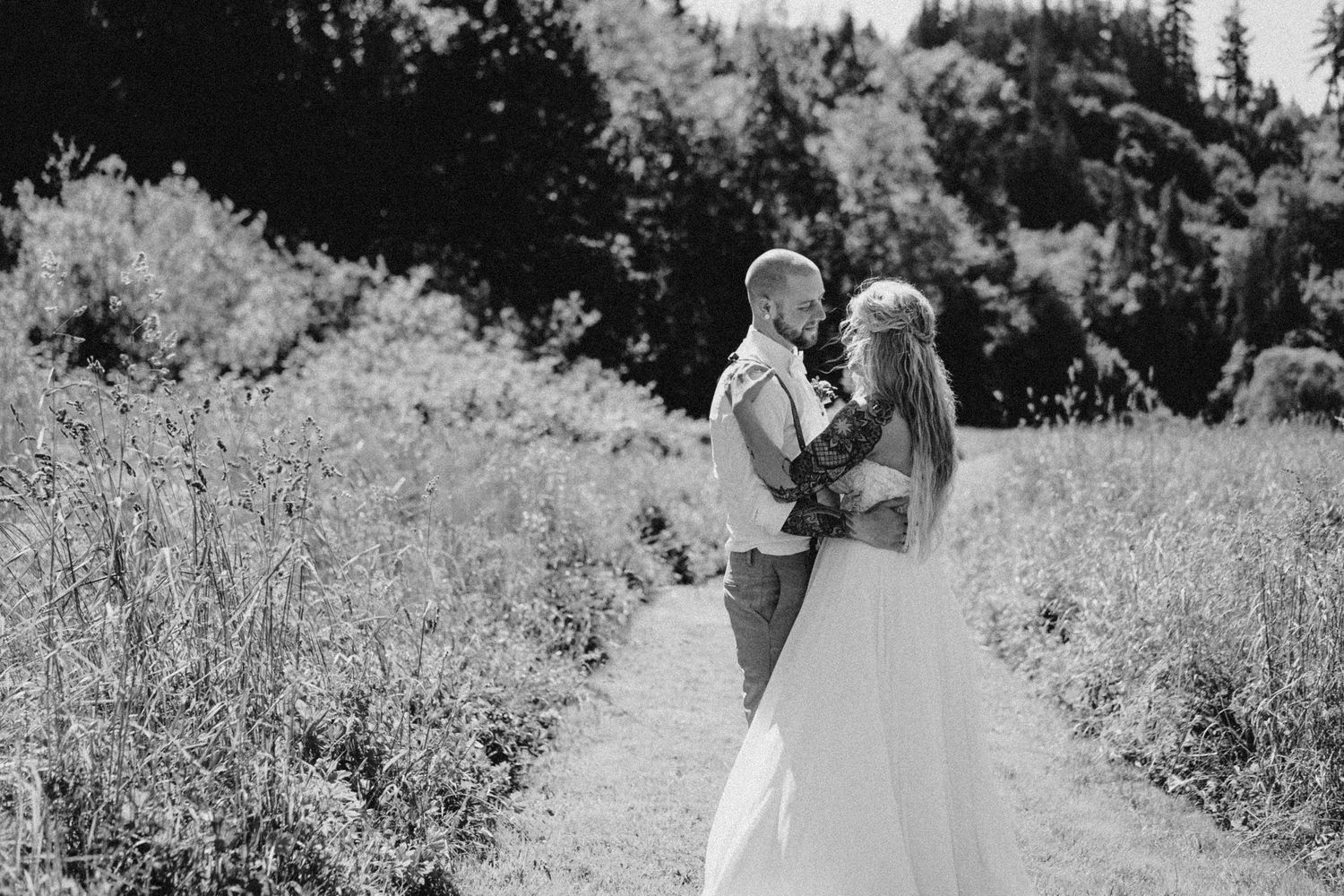 Black and white 35mm film portrait of bride and groom dancing in field of tall grass, cinematic editorial wedding photography