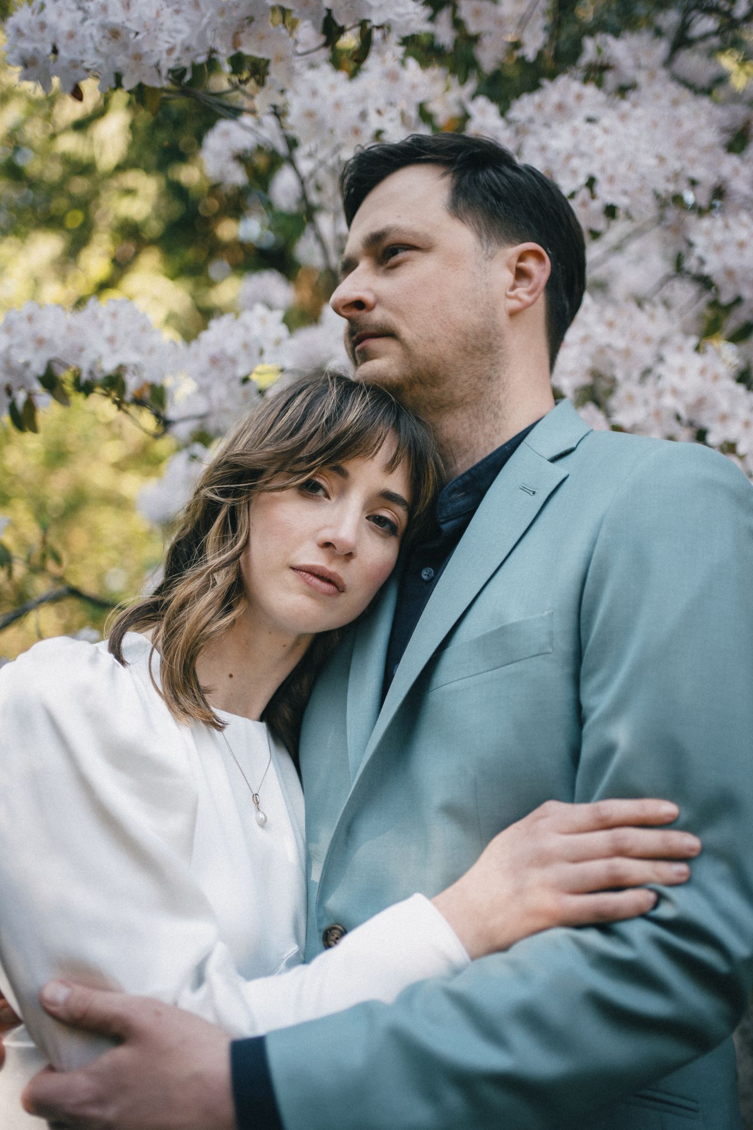 Intimate Seattle engagement portrait with couple embracing among cherry blossoms, showcasing emotional connection and soft natural lighting