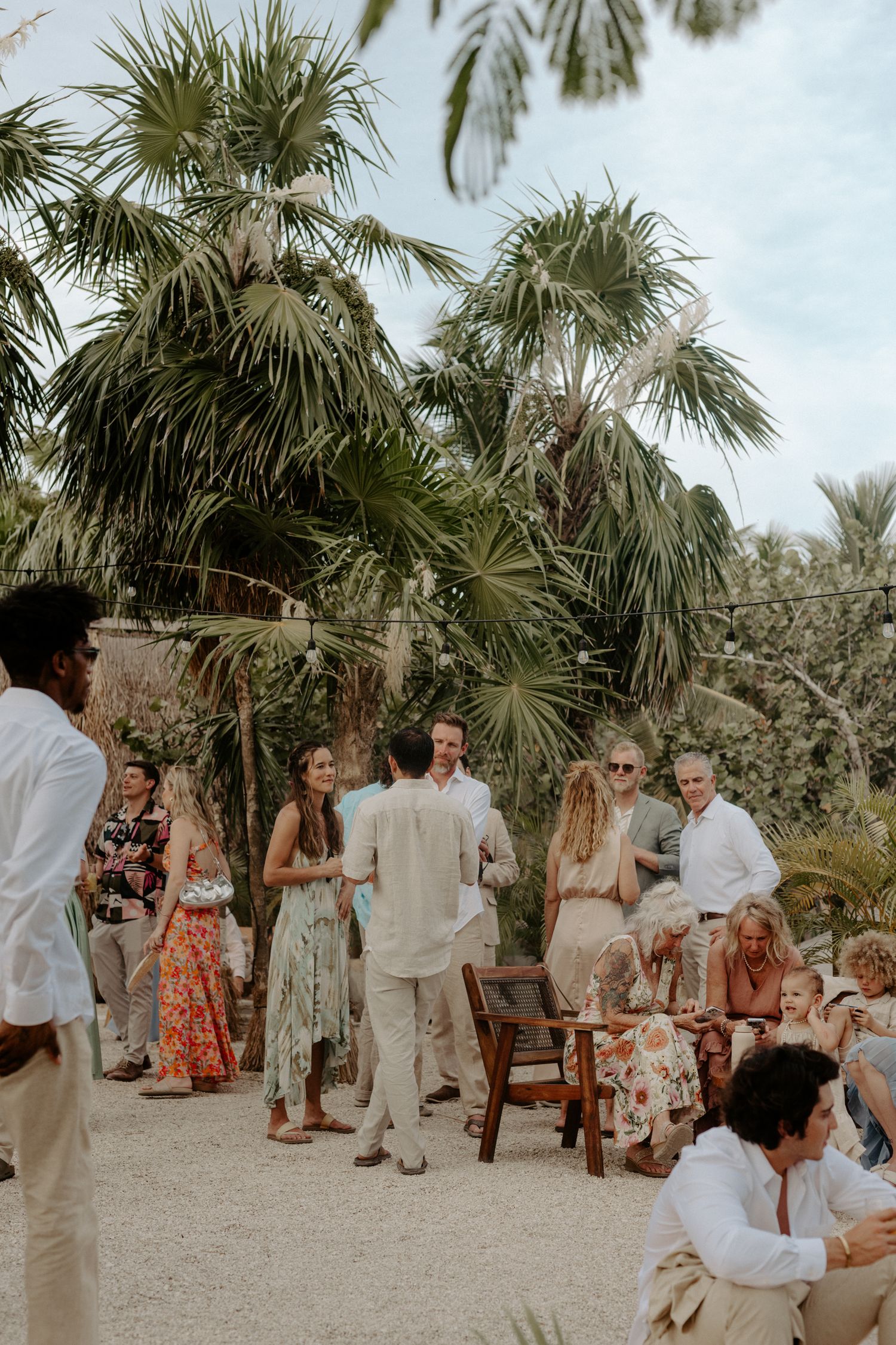Outdoor Tulum wedding ceremony with couple and guests gathered under palm trees, showcasing natural beachside setting of destination wedding