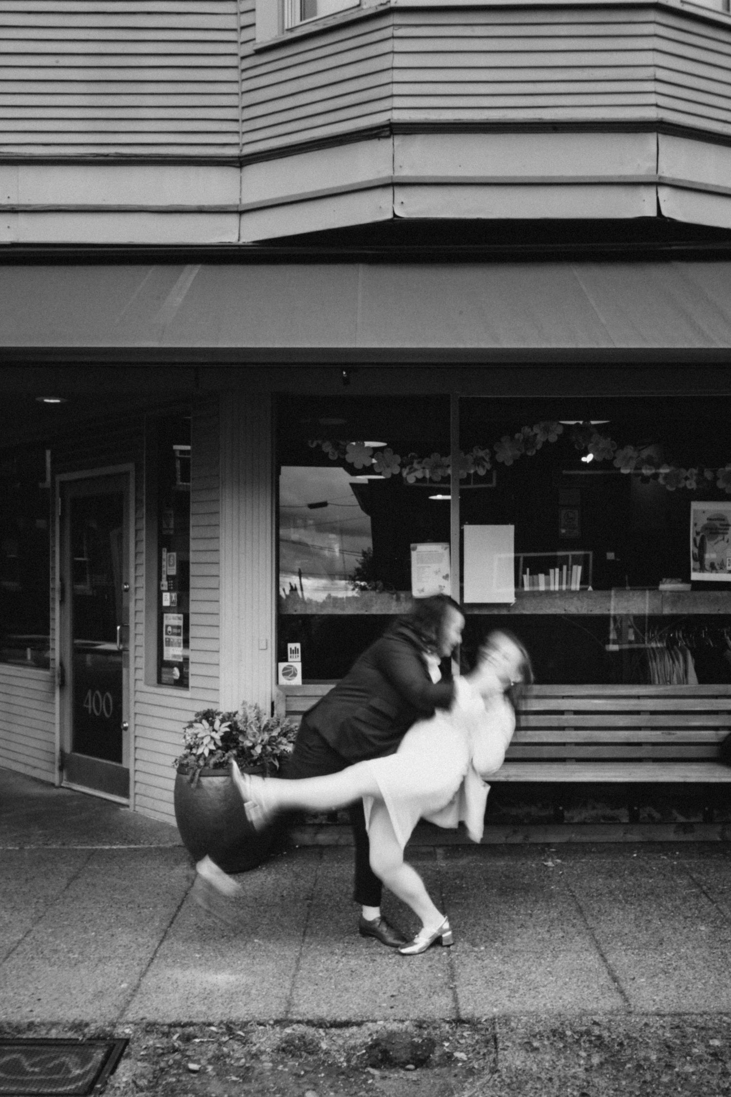 Black and white intimate Fremont elopement portrait with groom dipping bride in front of Seattle storefront, showcasing joy in urban setting