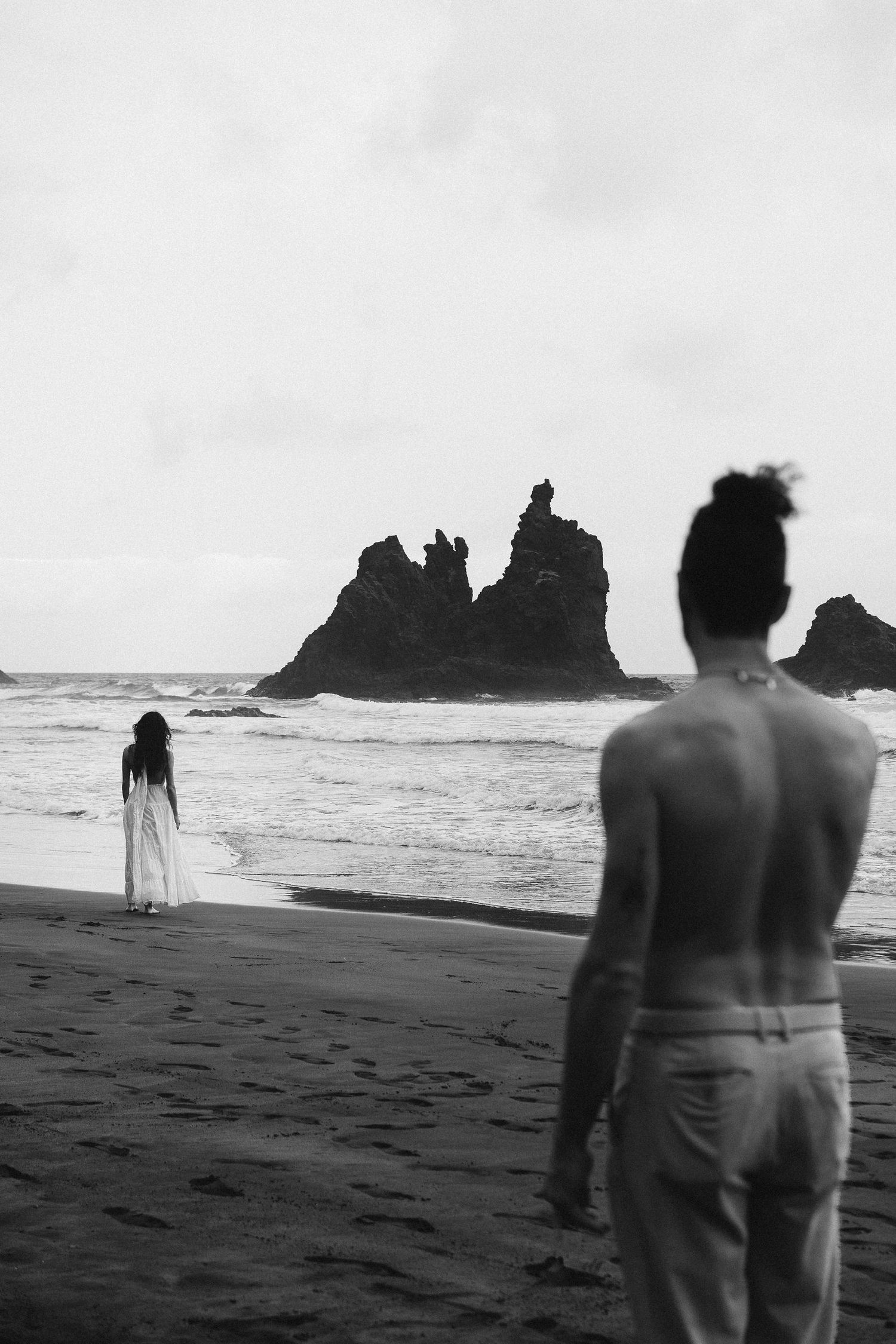 Black and white beach portrait from behind in Tenerife, intimate 35mm film engagement photography featuring distant rocky formations