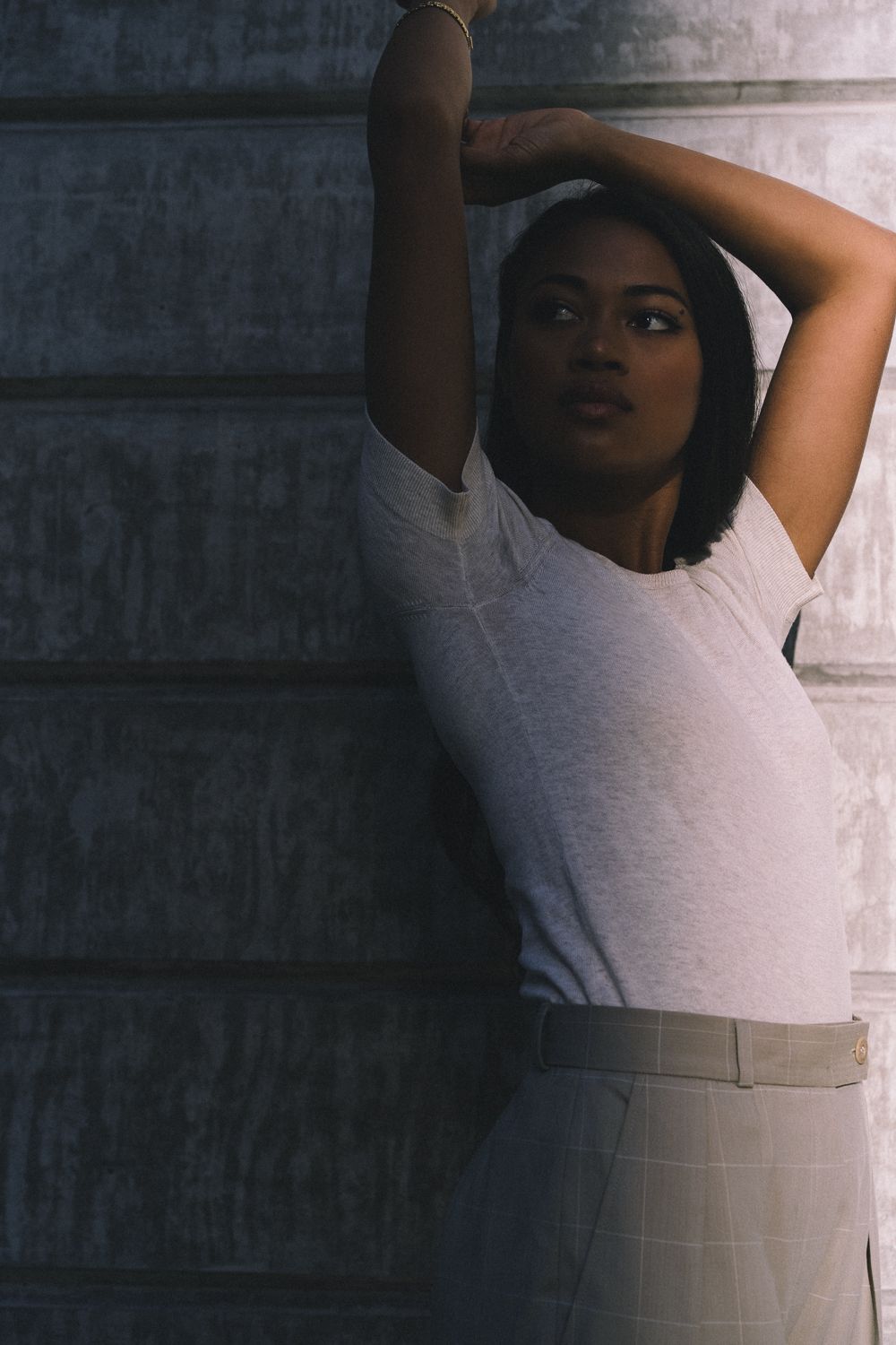 Minimalist color portrait with arms raised against textured wall, Seattle film photography with cinematic fashion approach